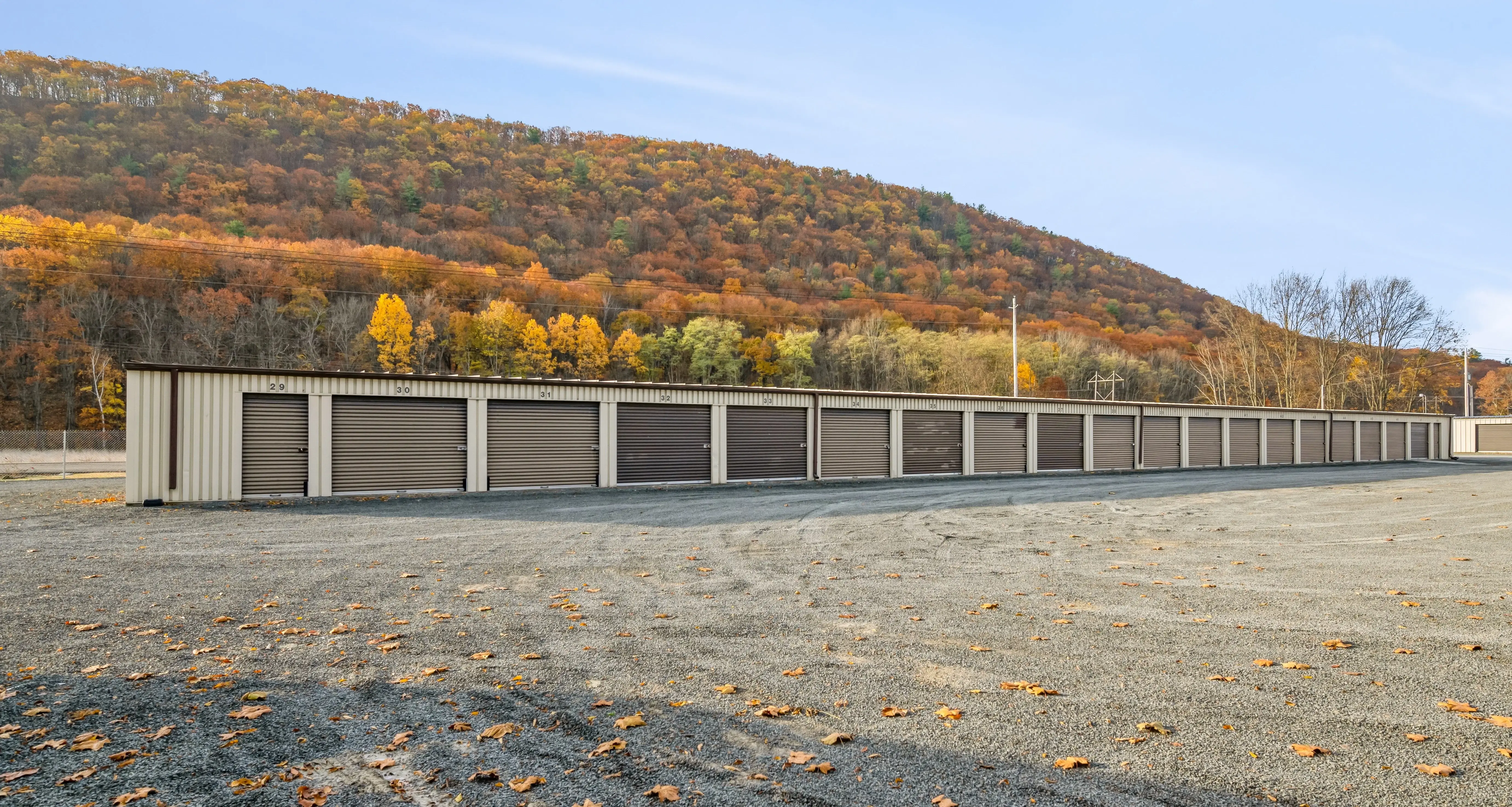 Row of drive up storage units with tan doors beside gravel driveway in Elmira NY