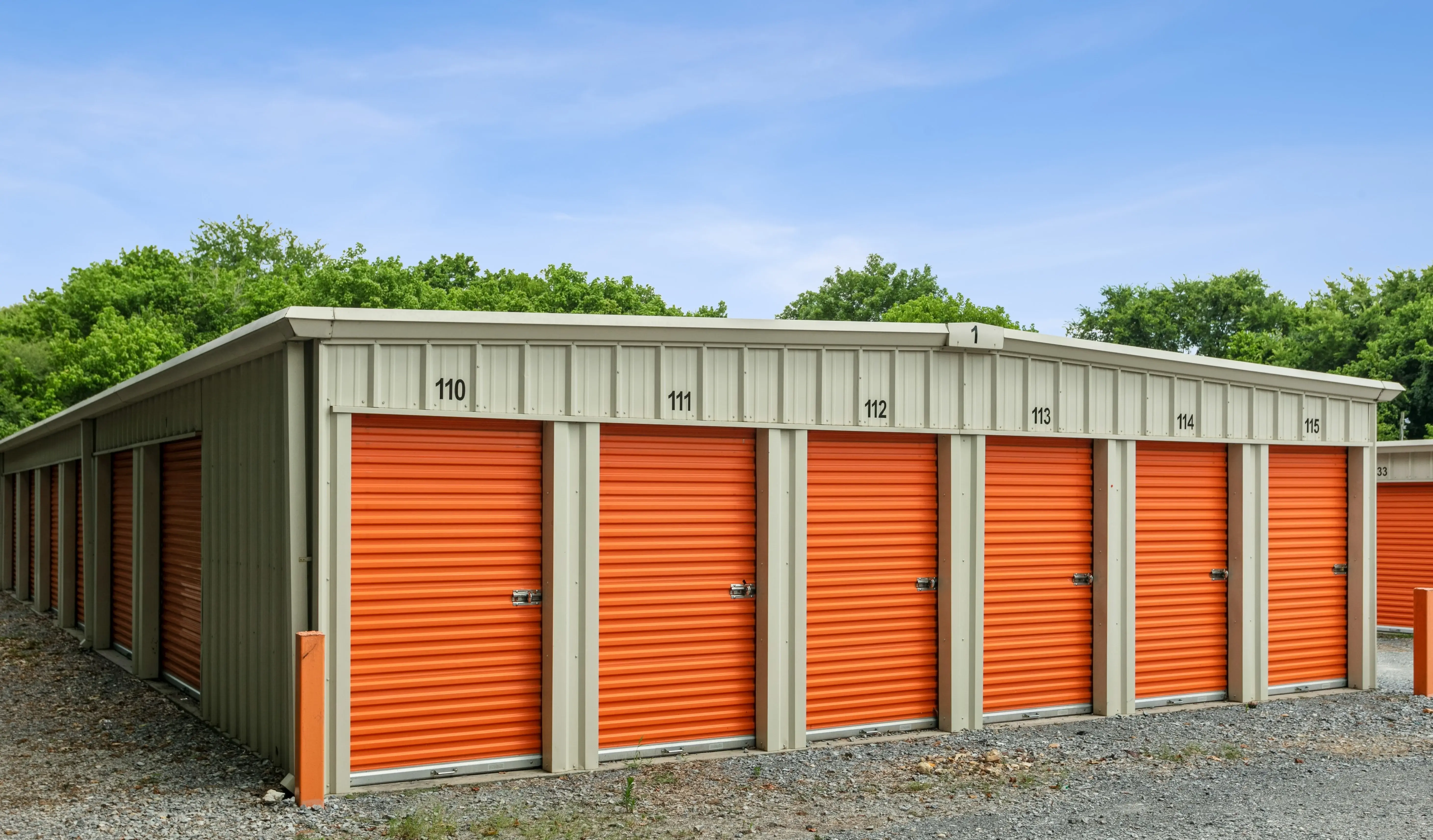 Corner view of a long storage building featuring bright orange roll up doors and a gravel driveway in Trion GA