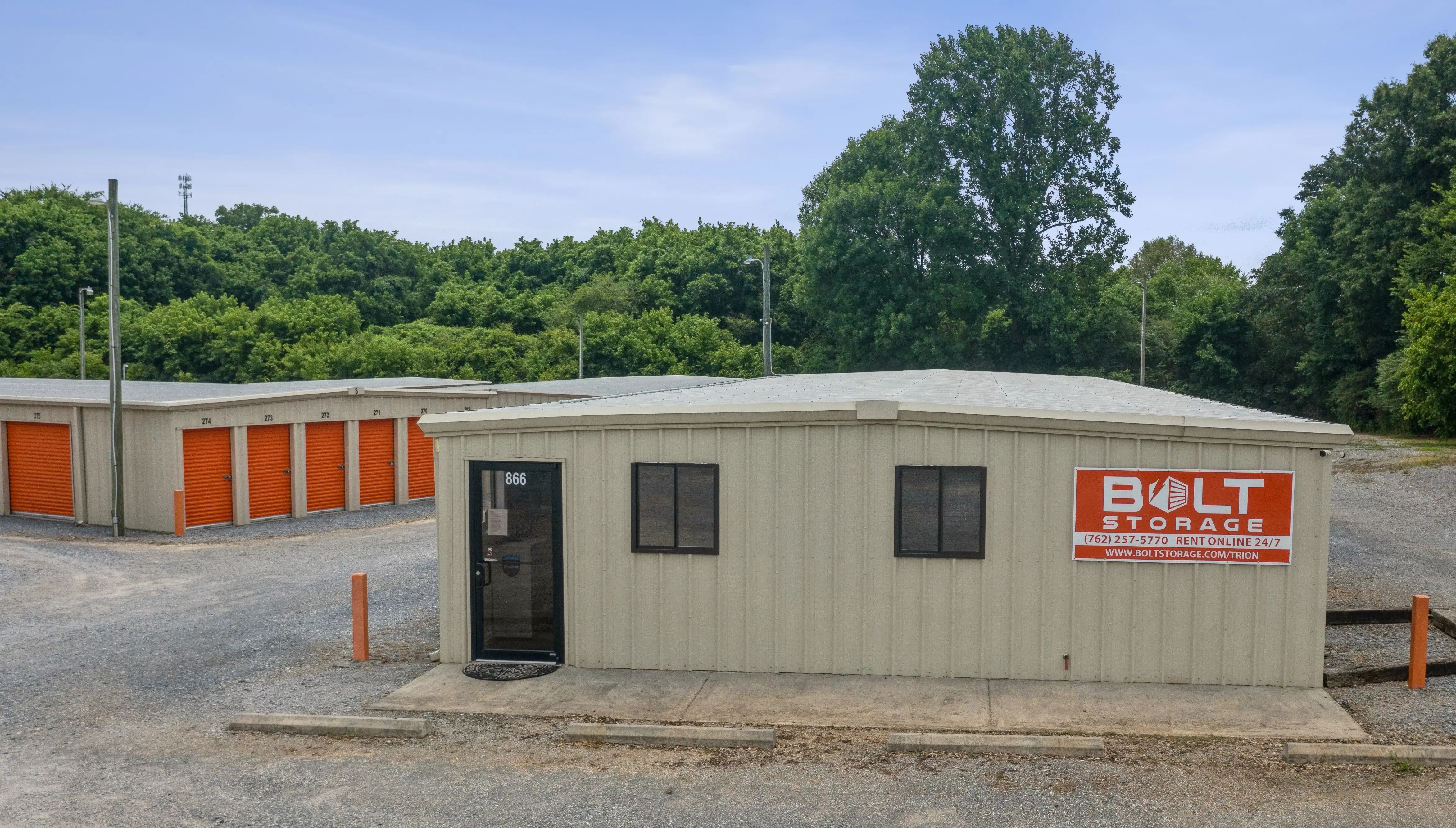 Small onsite office building with signage beside rows of orange door storage units in Trion GA