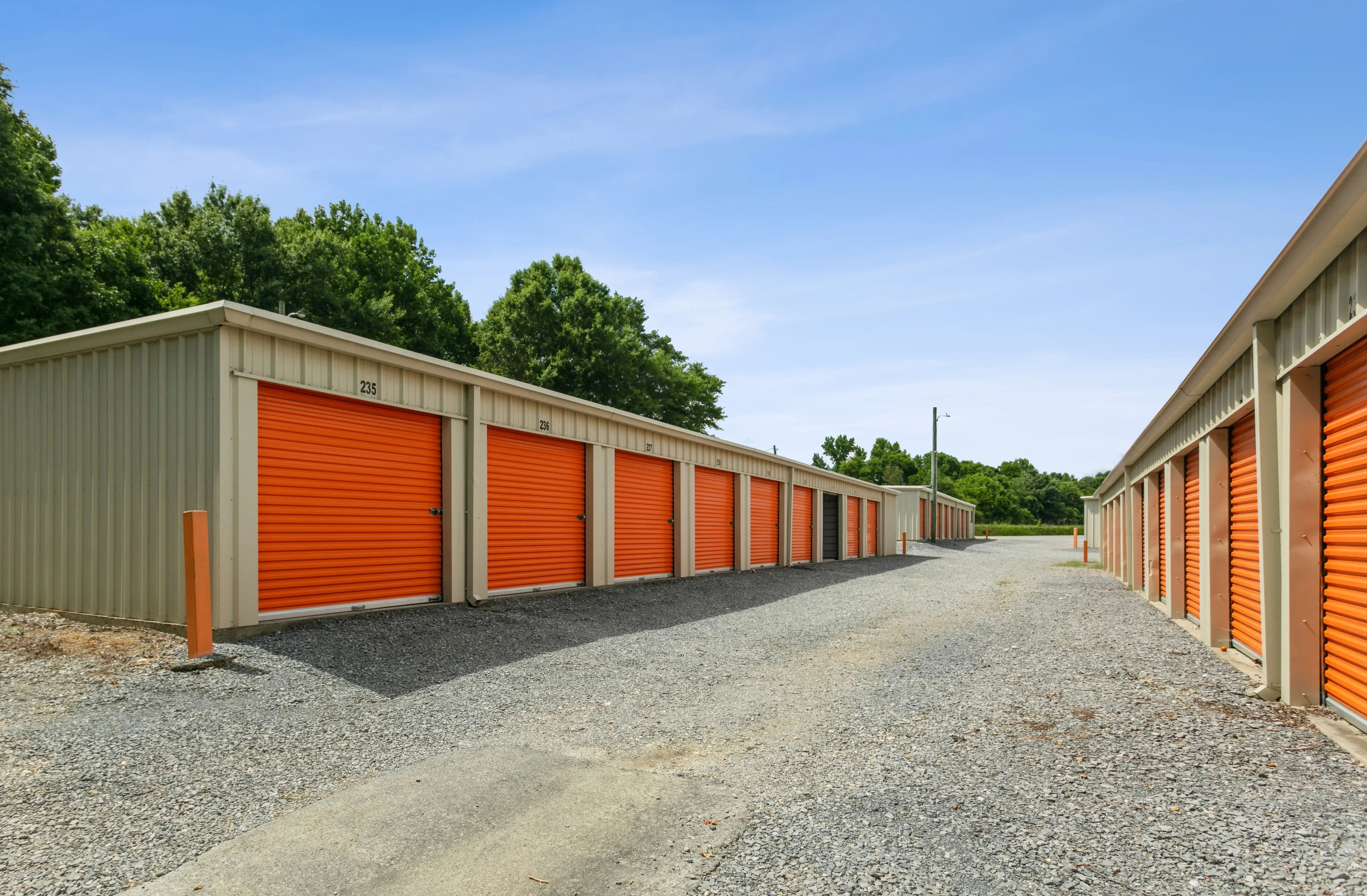 Row of orange roll up storage units along a narrow gravel lane bordered by trees in Trion GA