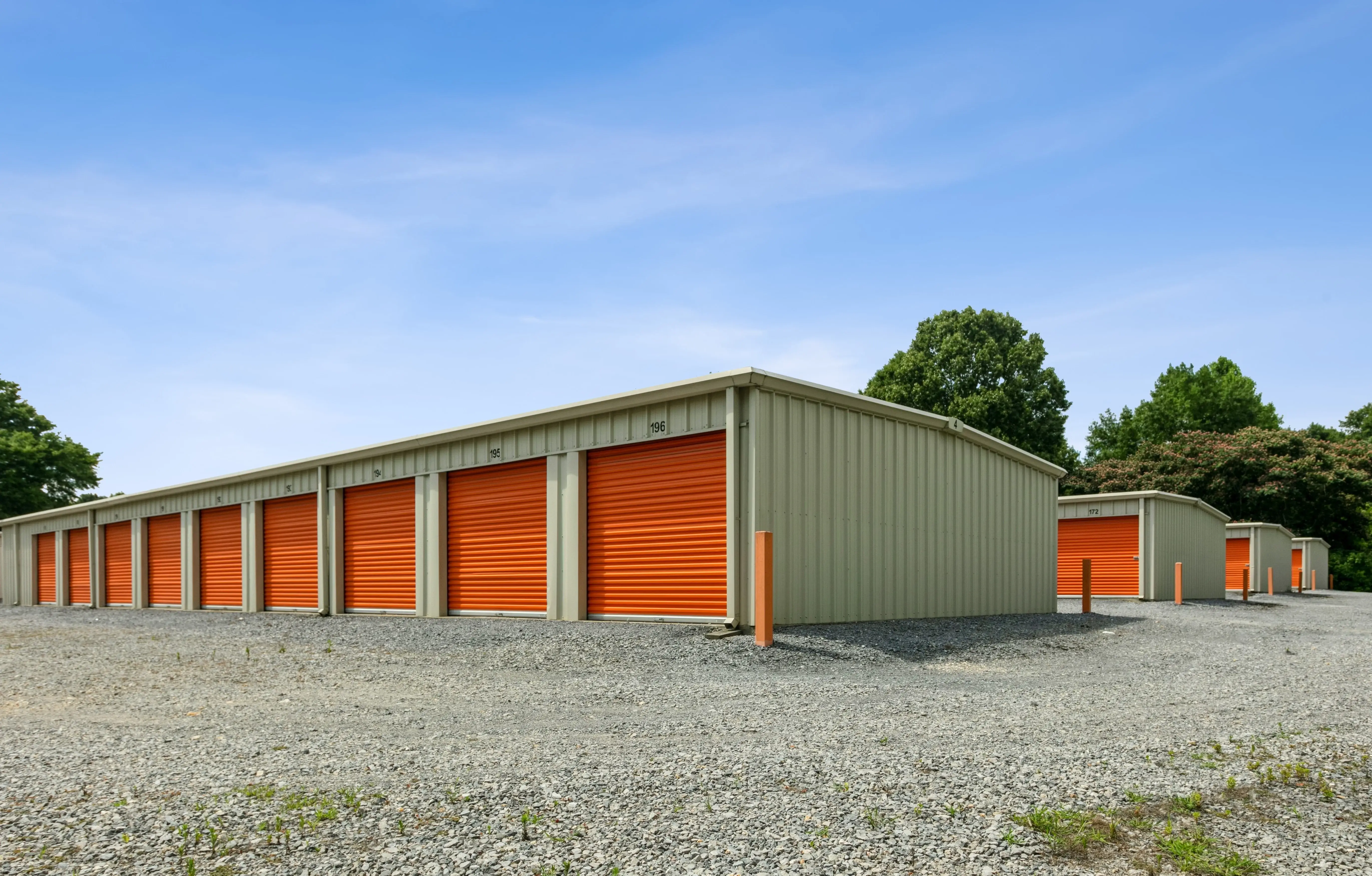 Angled perspective of drive up storage units with orange doors and a wide gravel approach at our Trion GA facility