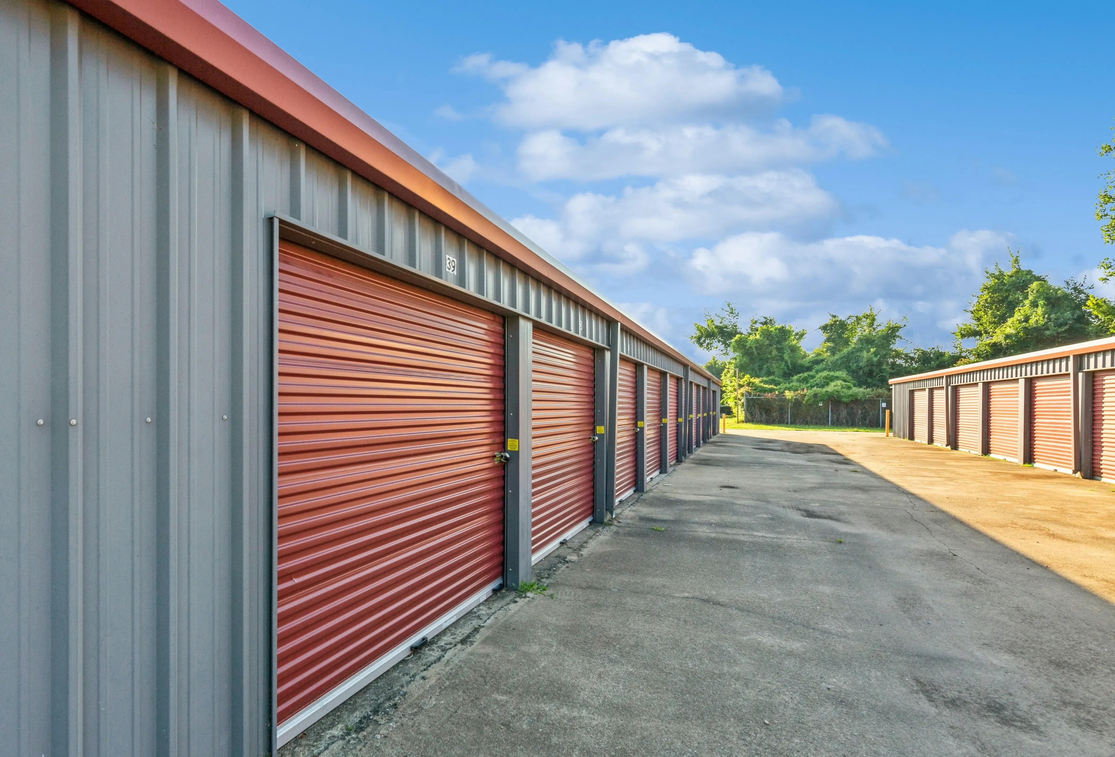 Row of red door storage units running along a paved driveway with bollards for protection in Walls MS
