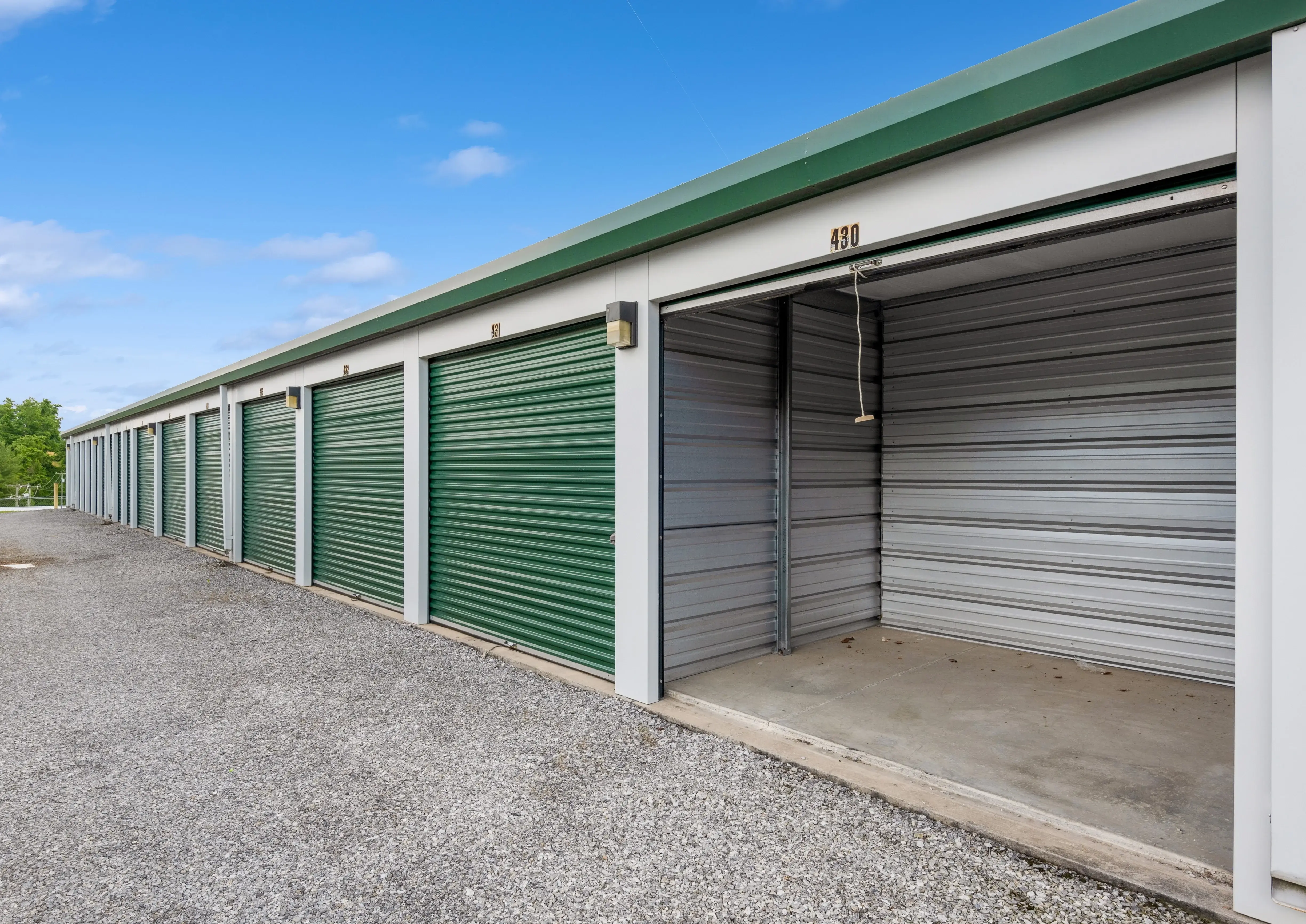 Drive up storage units with green doors along a gravel driveway in Abingdon VA, with one unit open showing the interior