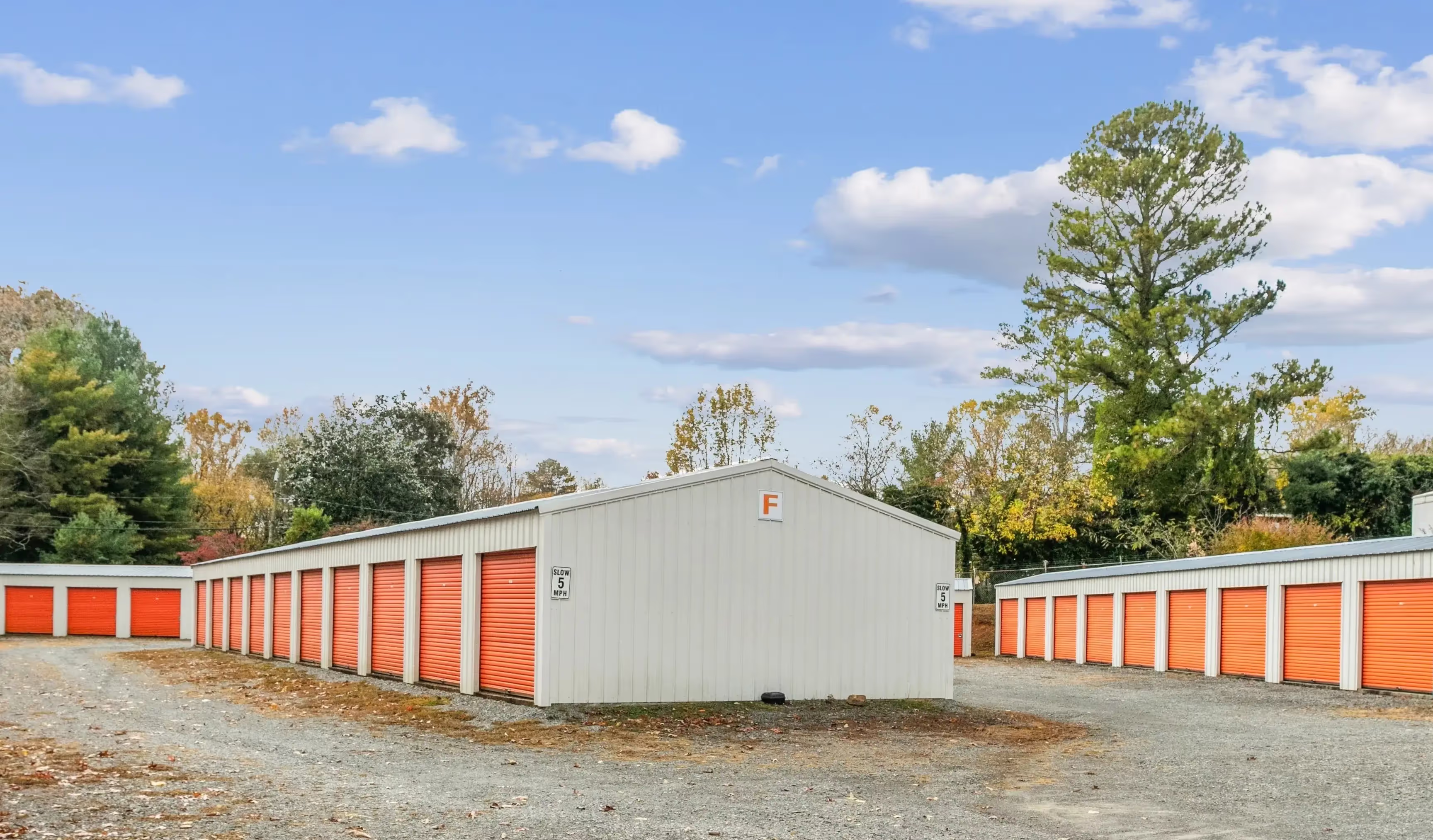 Exterior view of multiple drive up storage buildings with orange roll up doors in Ellijay GA
