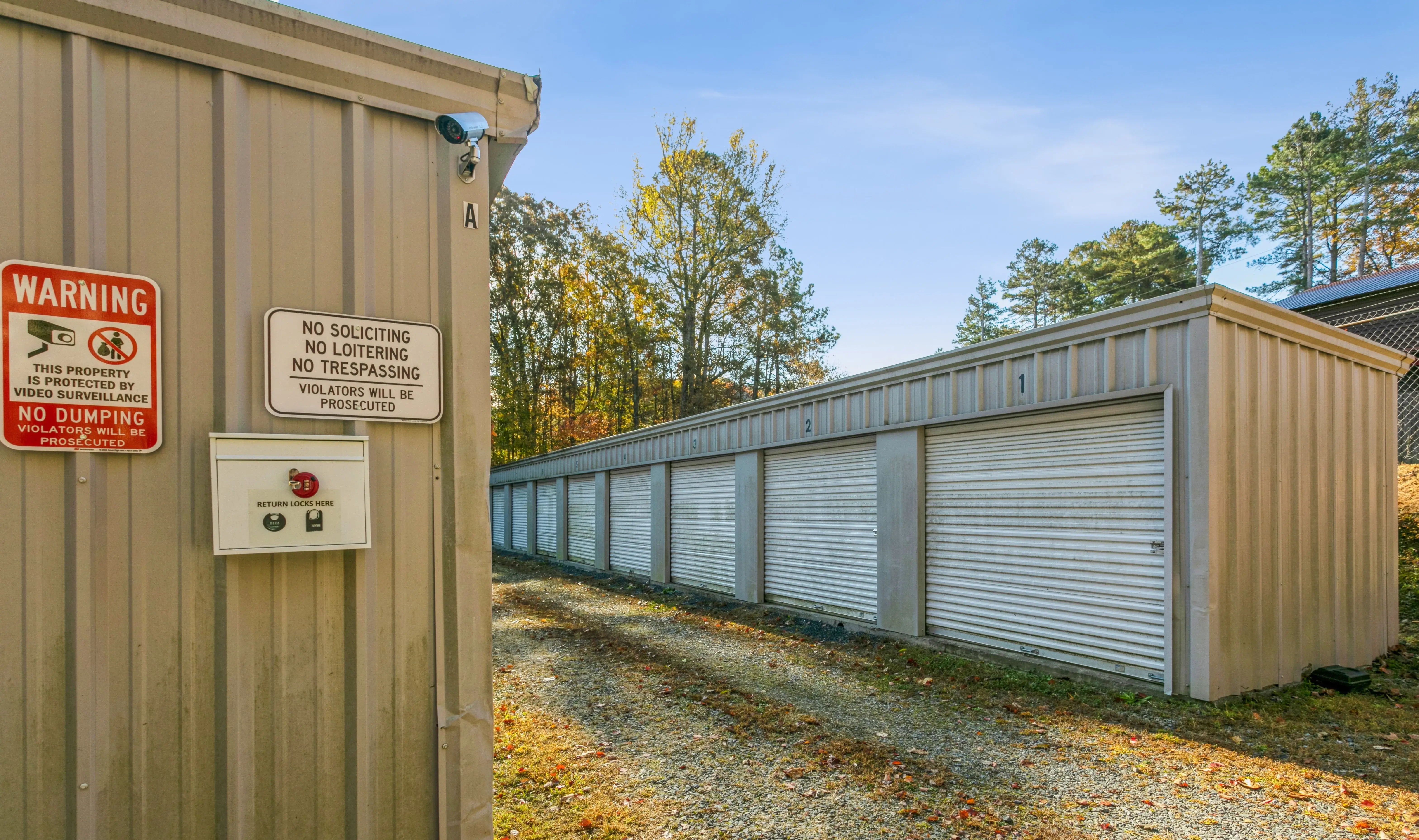 Exterior view of drive up storage units with white roll up doors along gravel driveway at our Ellijay GA facility