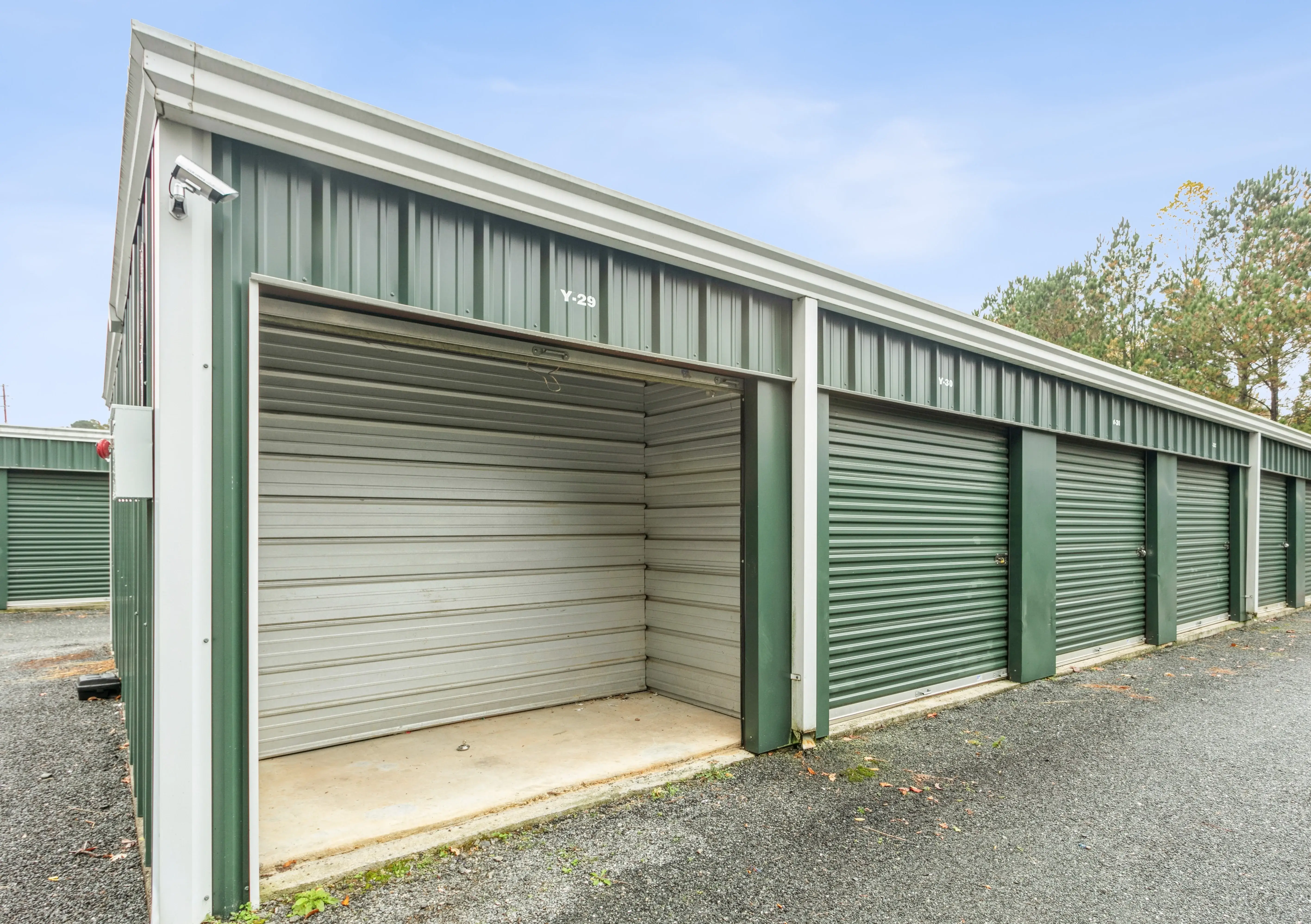 Corner view of a storage building in Ellijay GA showing green roll up doors and a gravel turnaround area