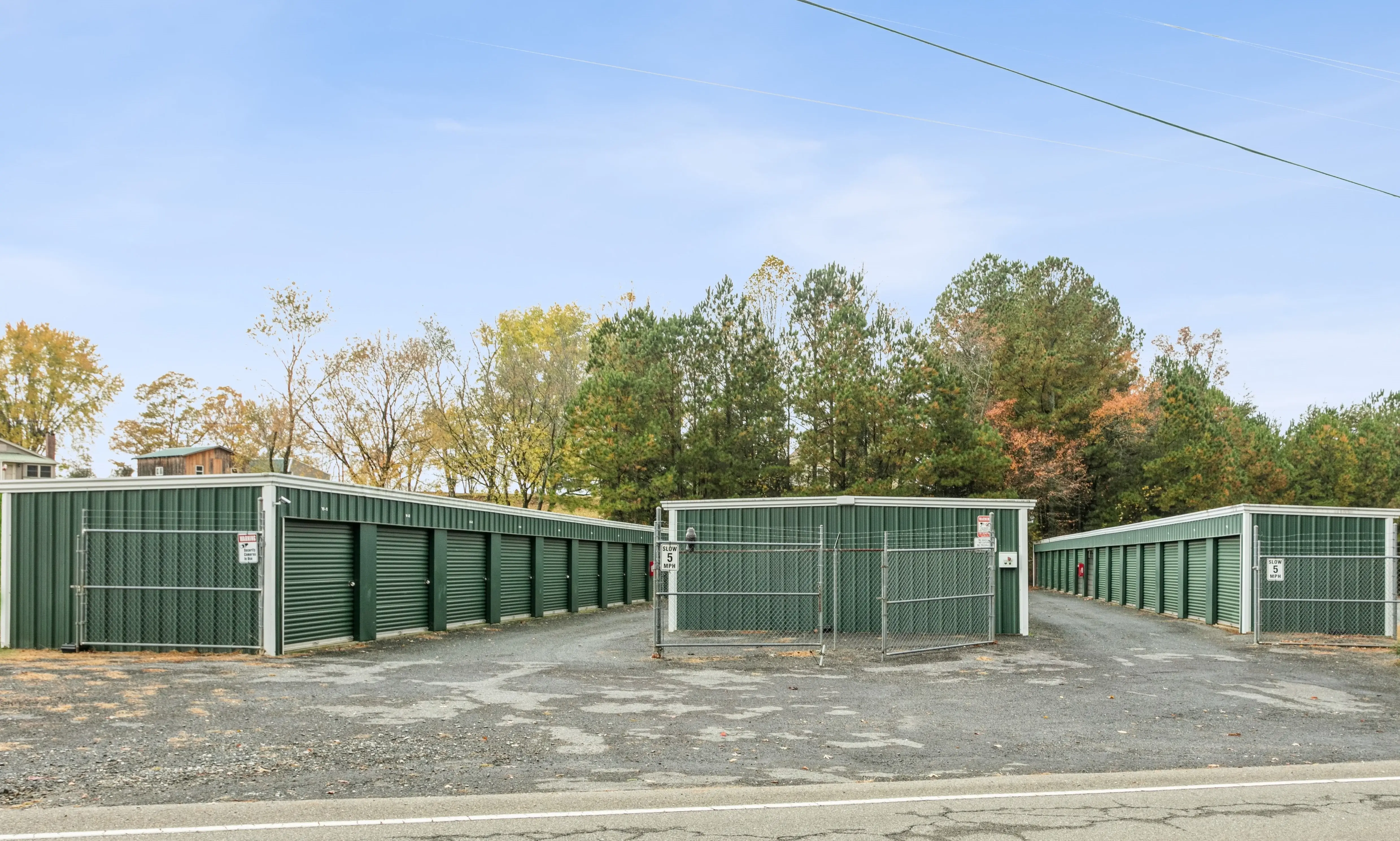 Wide front view of a long stretch of storage units with green doors on a gravel lot in Ellijay GA