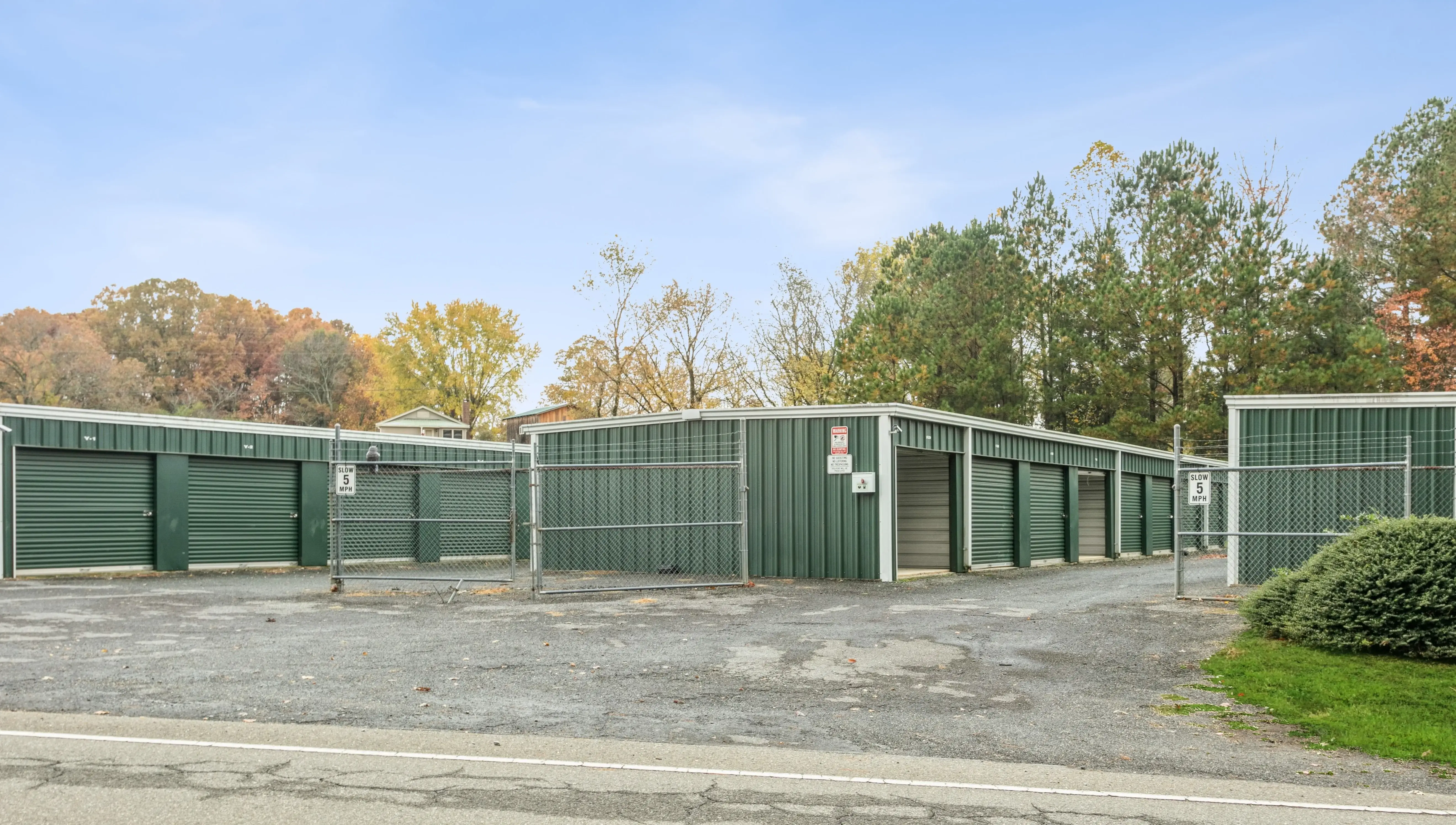 Front-facing view of storage buildings with green roll up doors and fall foliage in the background in Ellijay GA