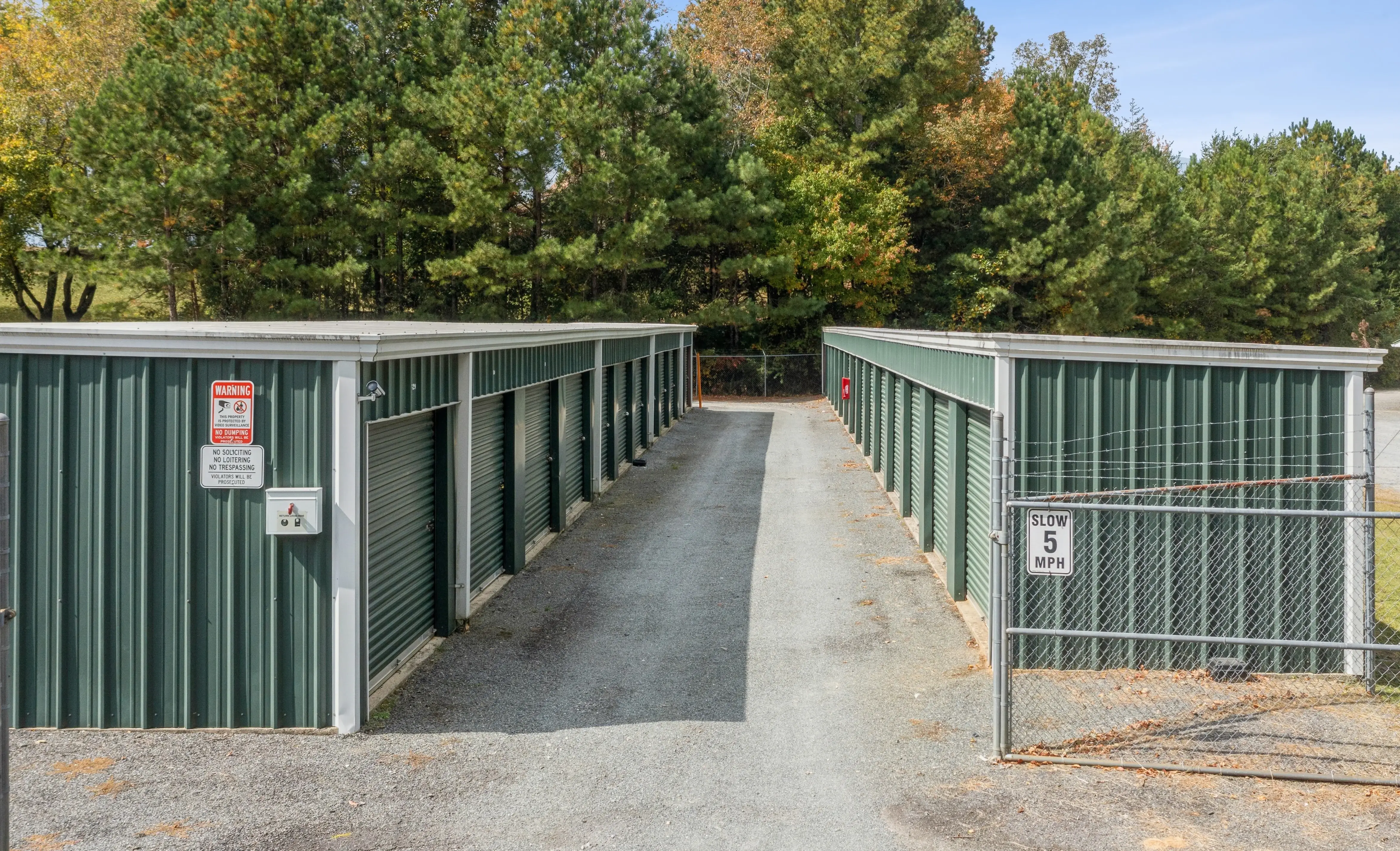 Secure gated entrance to our Ellijay GA storage facility with keypad access and green door storage units behind the fence