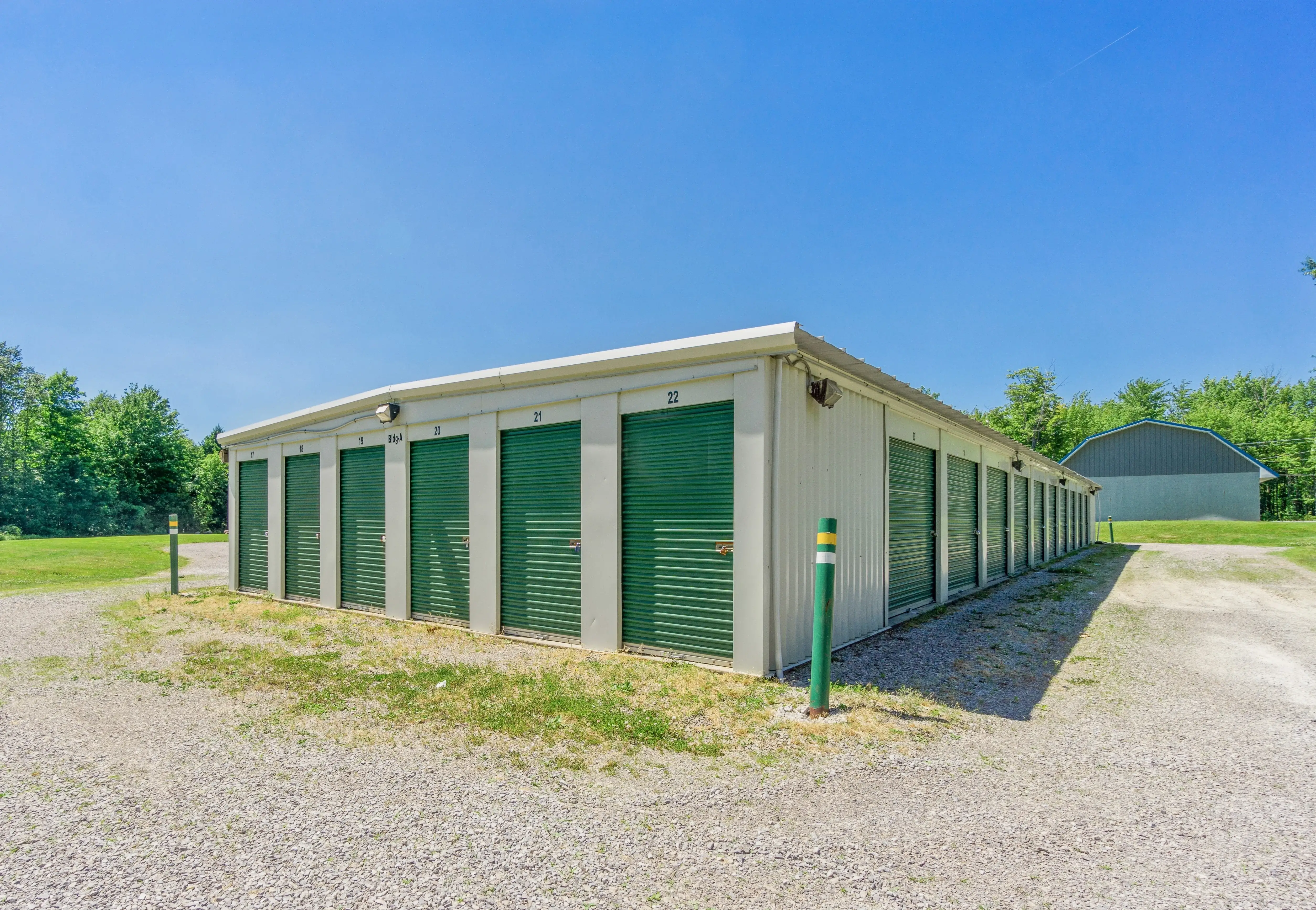 Exterior view of drive up storage buildings with green roll up doors and gravel driveway in McKean PA