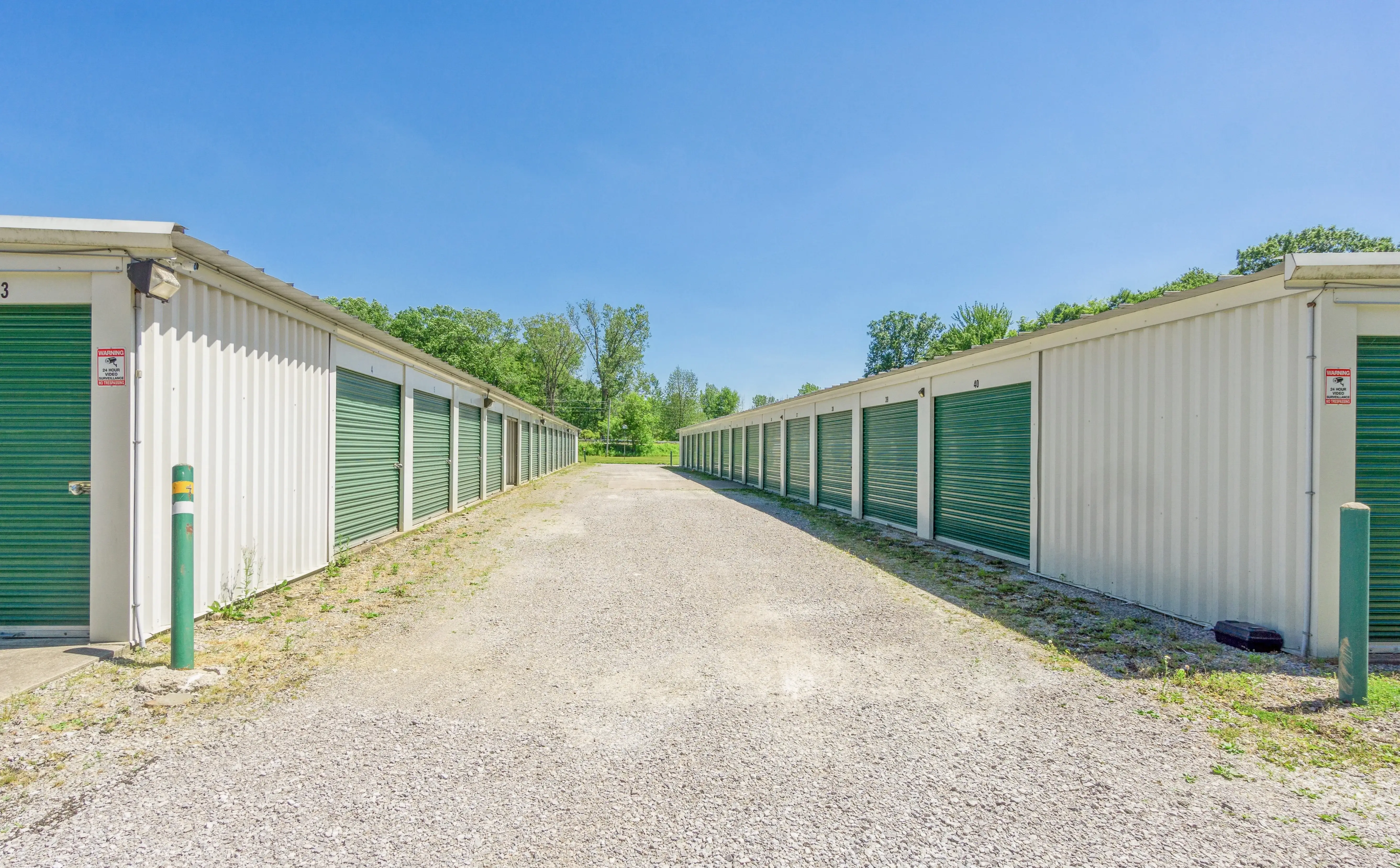 Row of drive up storage units with green doors along gravel access lane at our McKean PA location