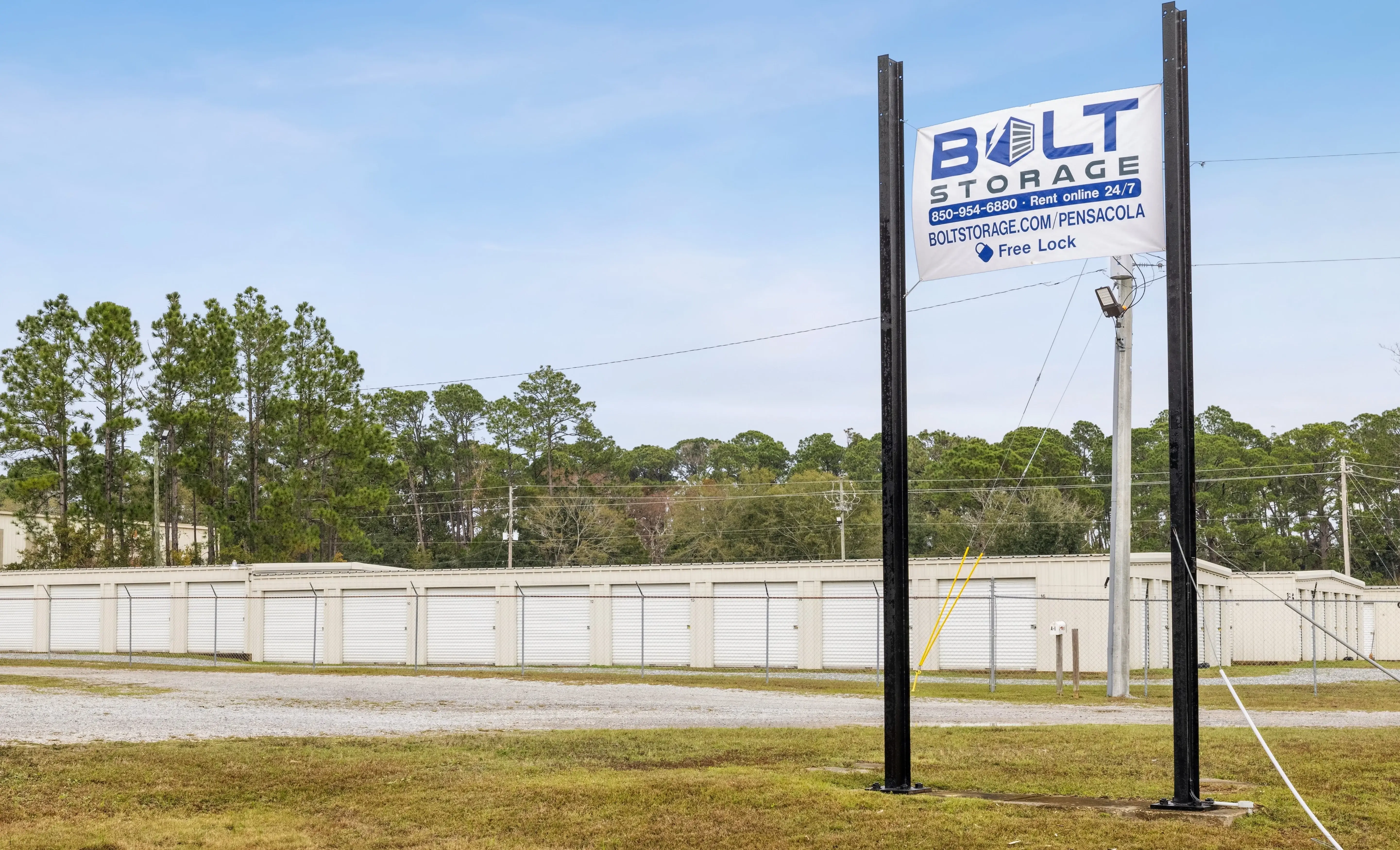Roadside sign for our Pensacola FL storage facility with white roll up units and fencing visible behind it