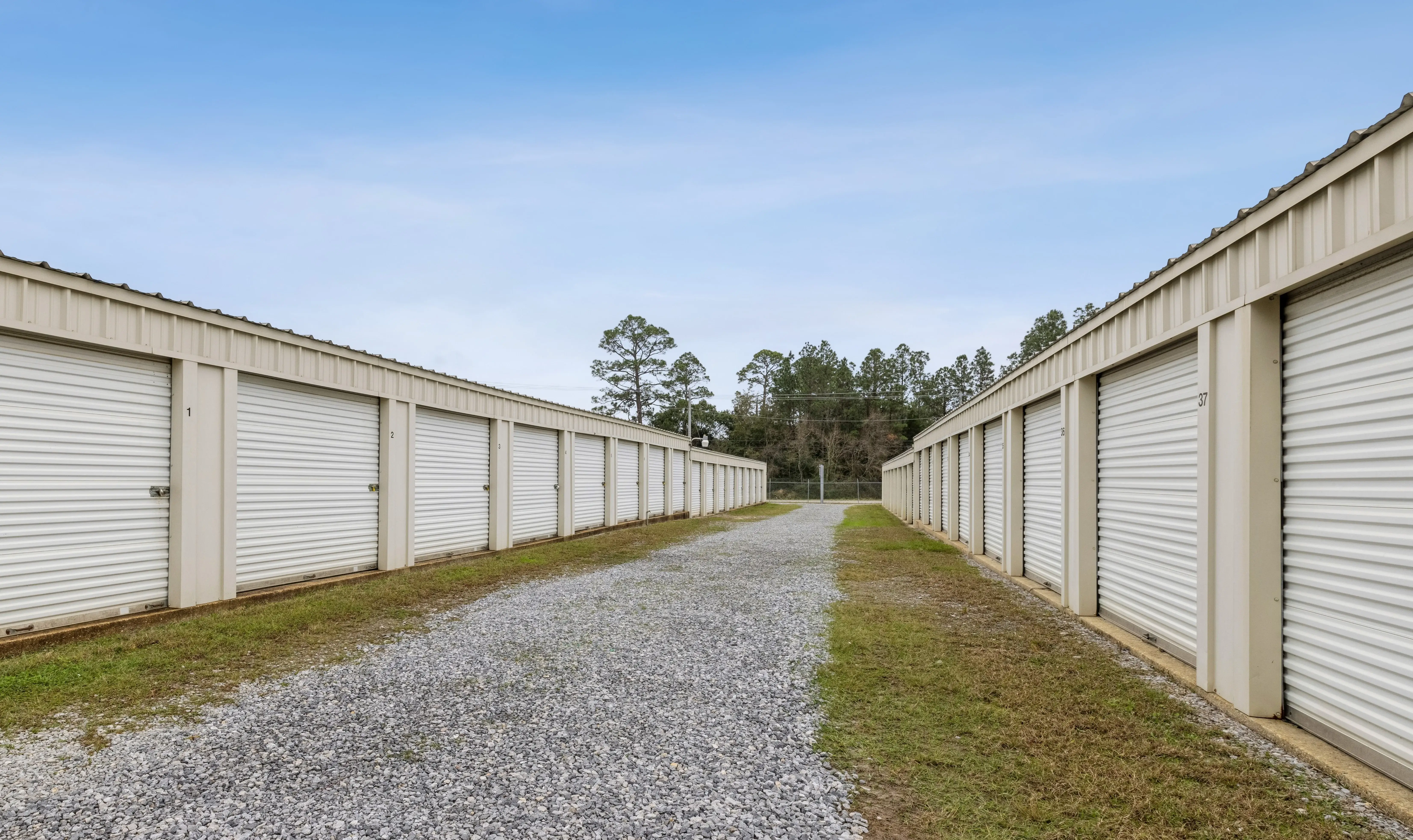 Narrow gravel lane between two rows of white storage units bordered by grass at our Pensacola FL facility