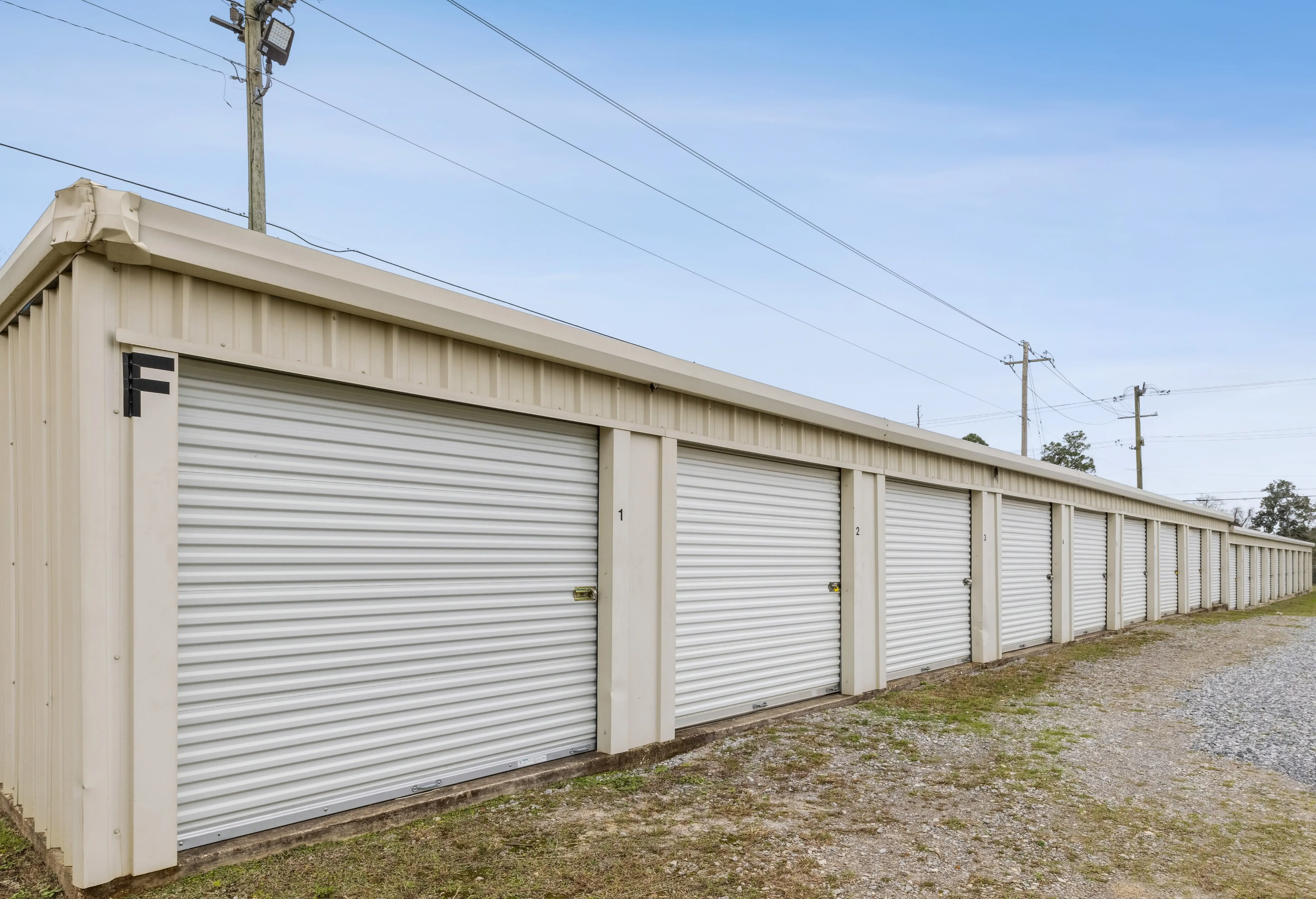 Side view of long storage building with white doors and overhead utility lines running alongside it in Pensacola FL