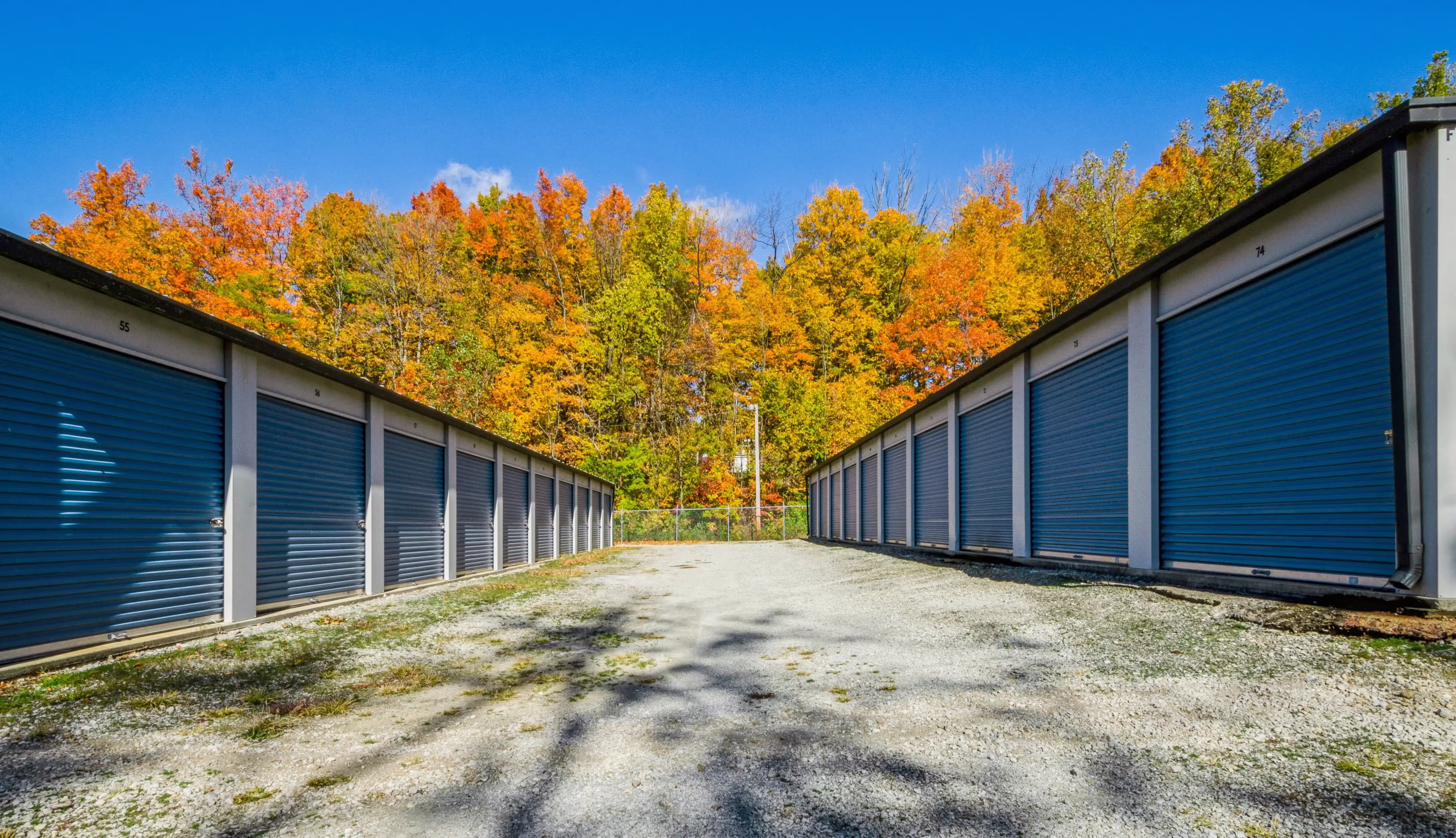 Storage buildings with blue roll up doors set against bright fall foliage along a gravel driveway in Peru IN