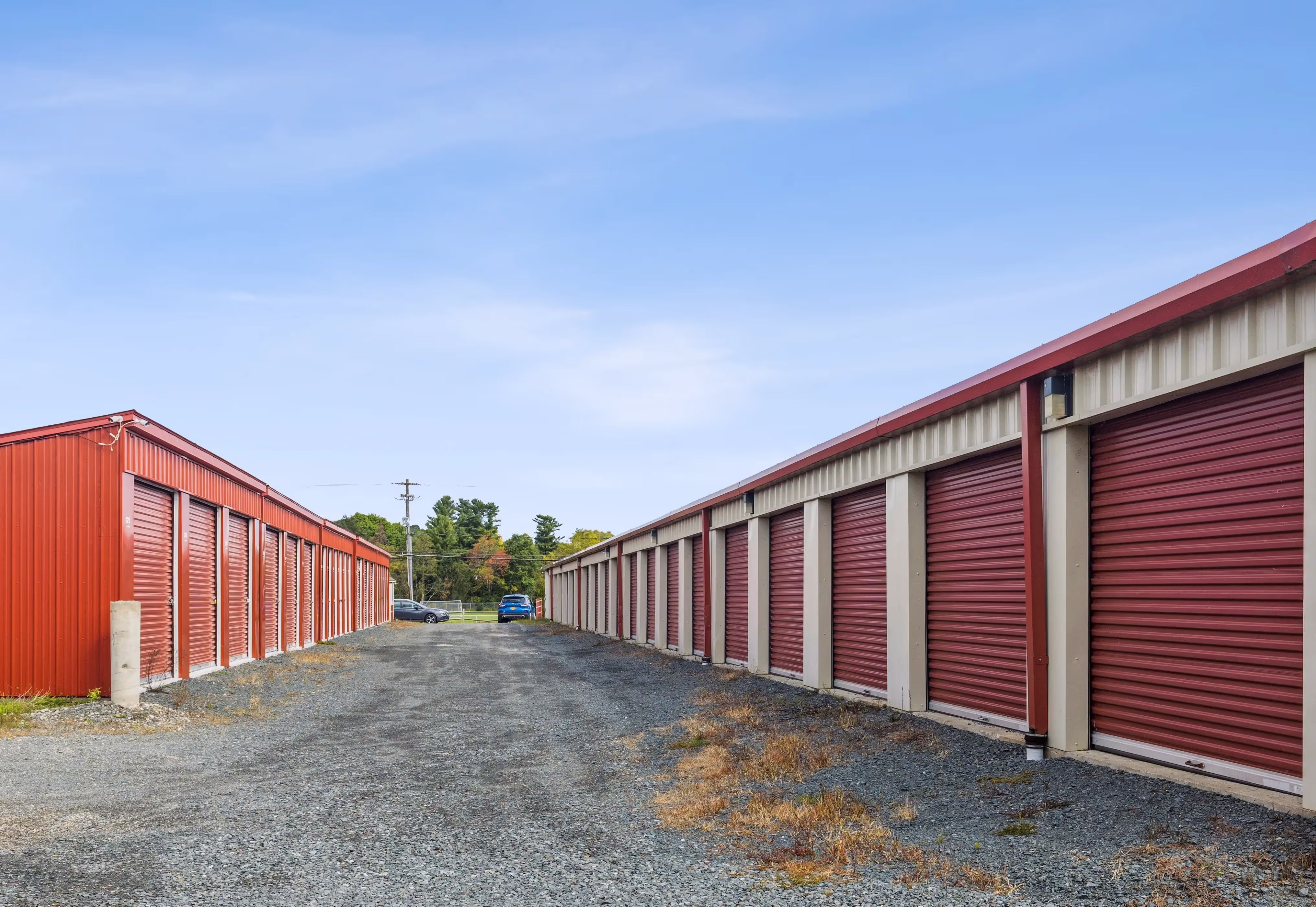 Row of drive up storage units with red roll up doors along a gravel driveway at our Troy NY facility