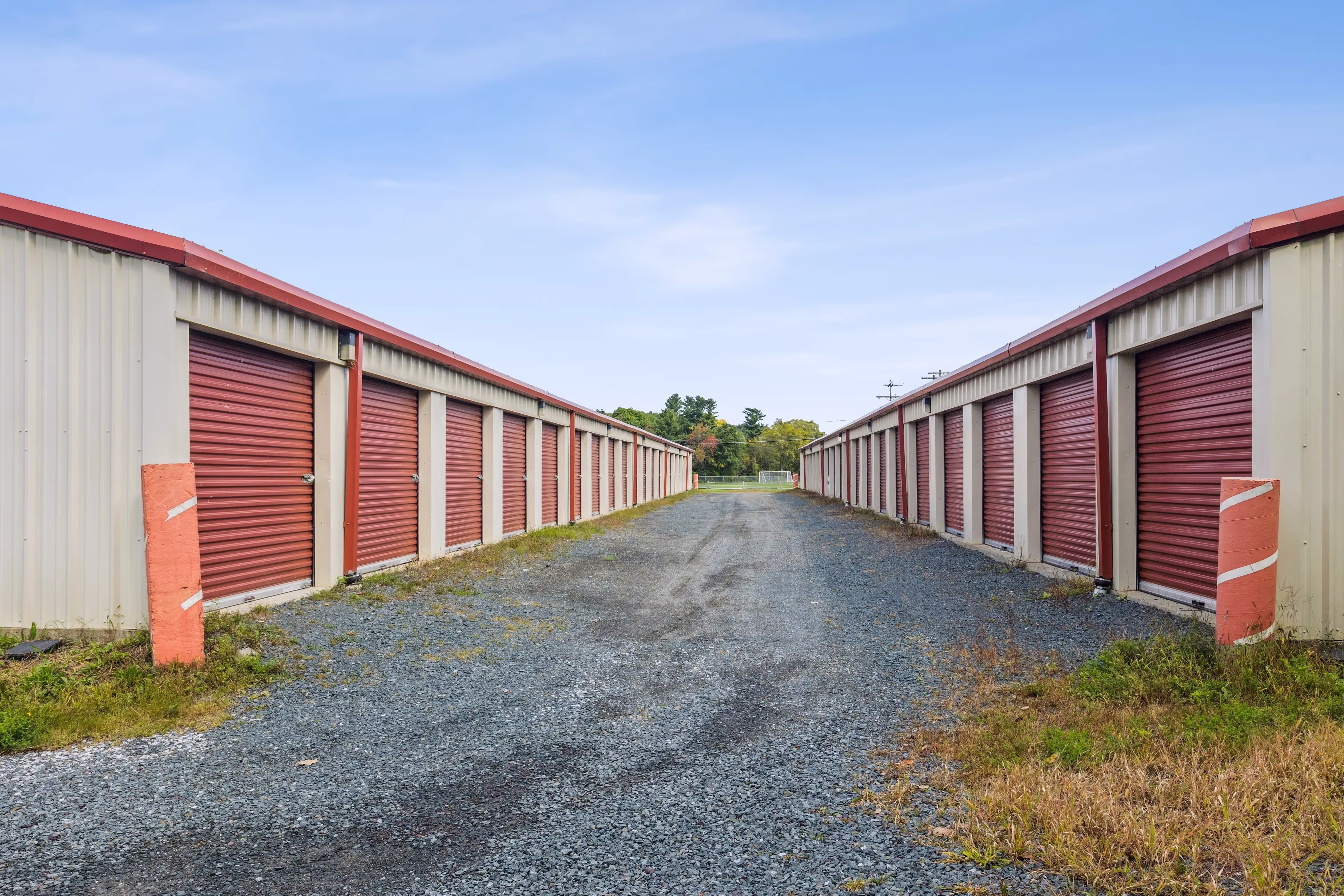 Drive up storage buildings with red doors and gravel access lanes in Troy NY