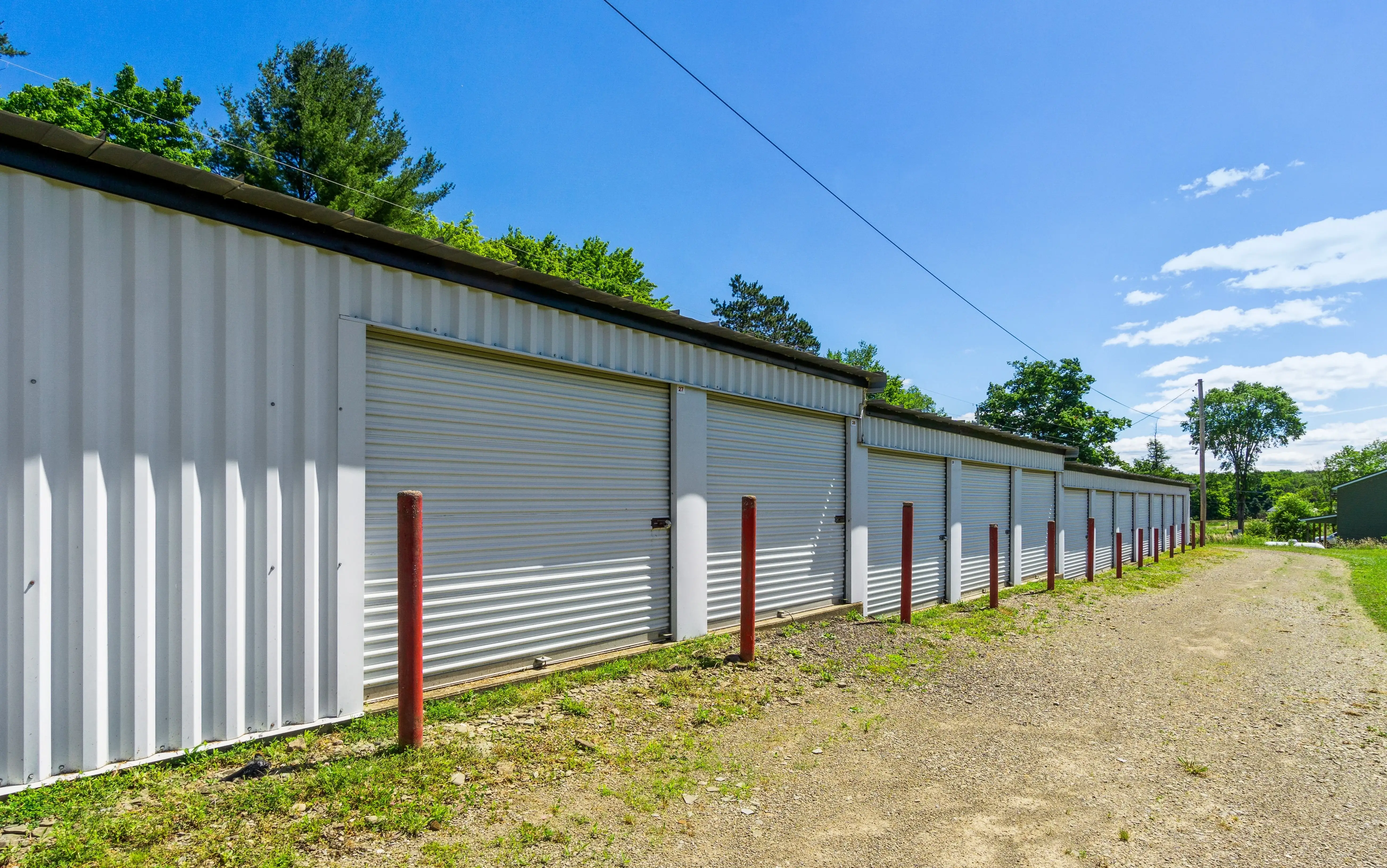 Long gravel drive running beside white storage buildings with metal siding and red corner posts at our Union City PA facility