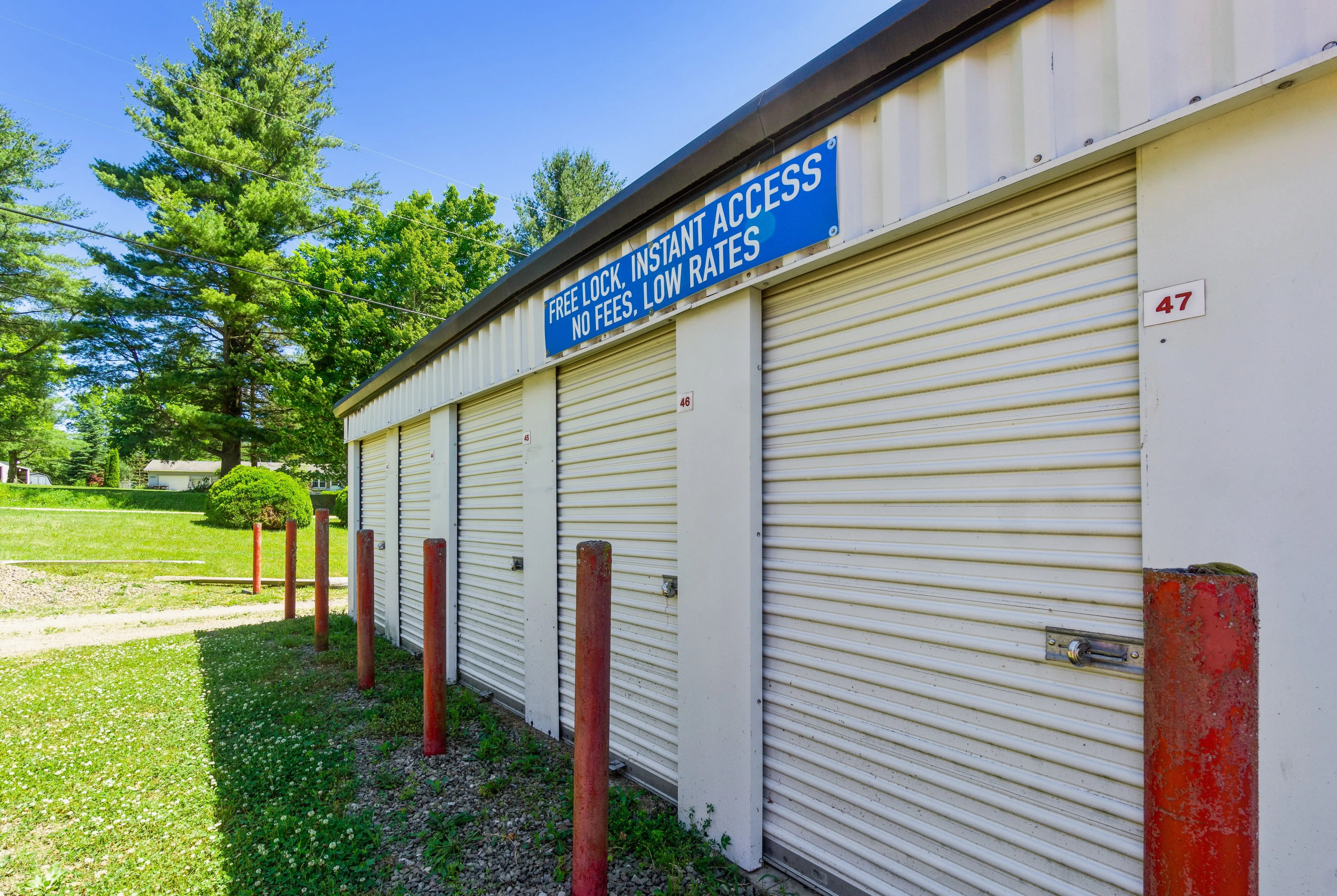 Front side of a storage building with white roll up doors and facility signage surrounded by grass and trees in Union City PA