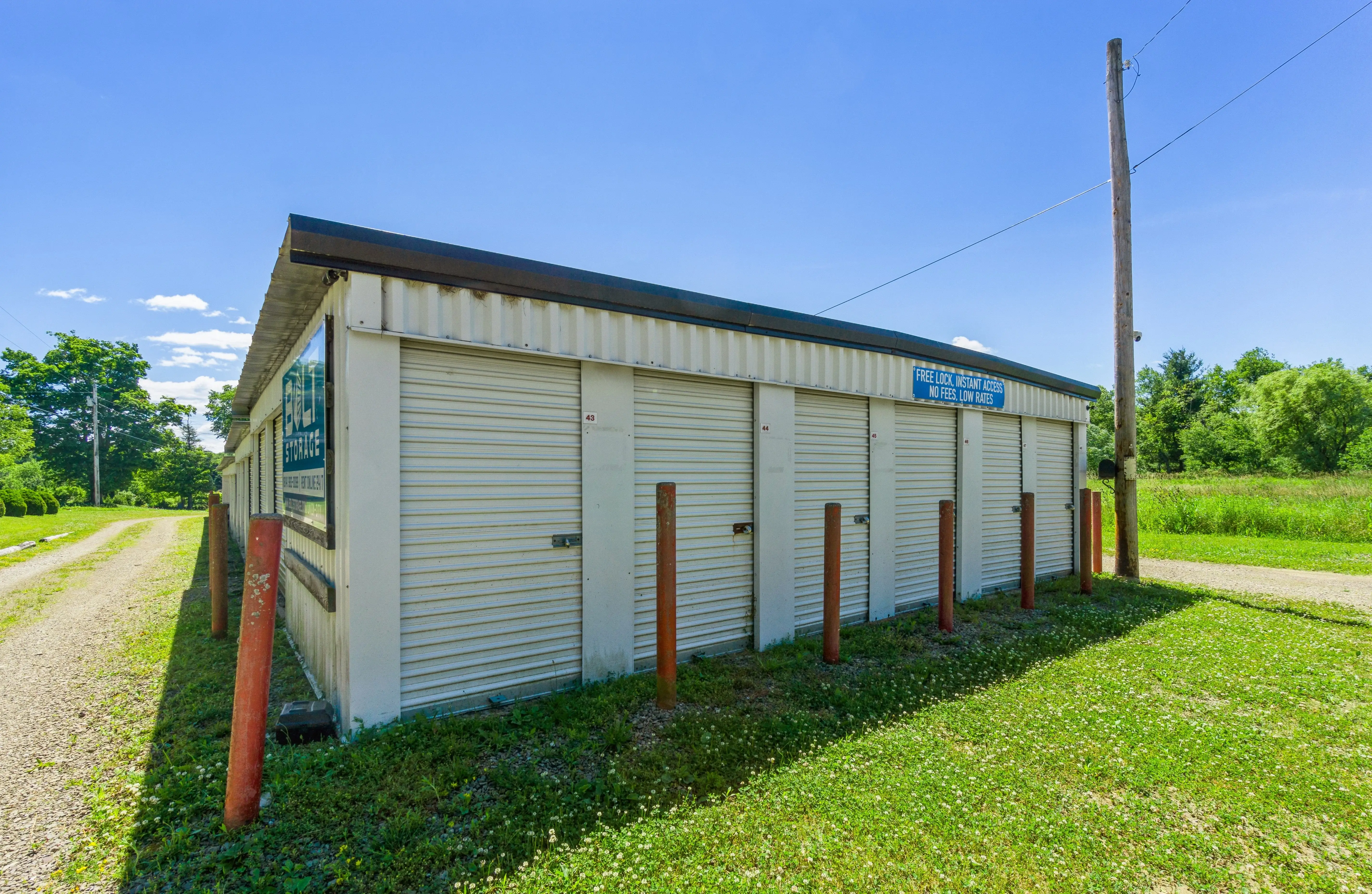Angled view of white storage buildings with red posts and a grassy slope leading to the main gravel driveway in Union City PA