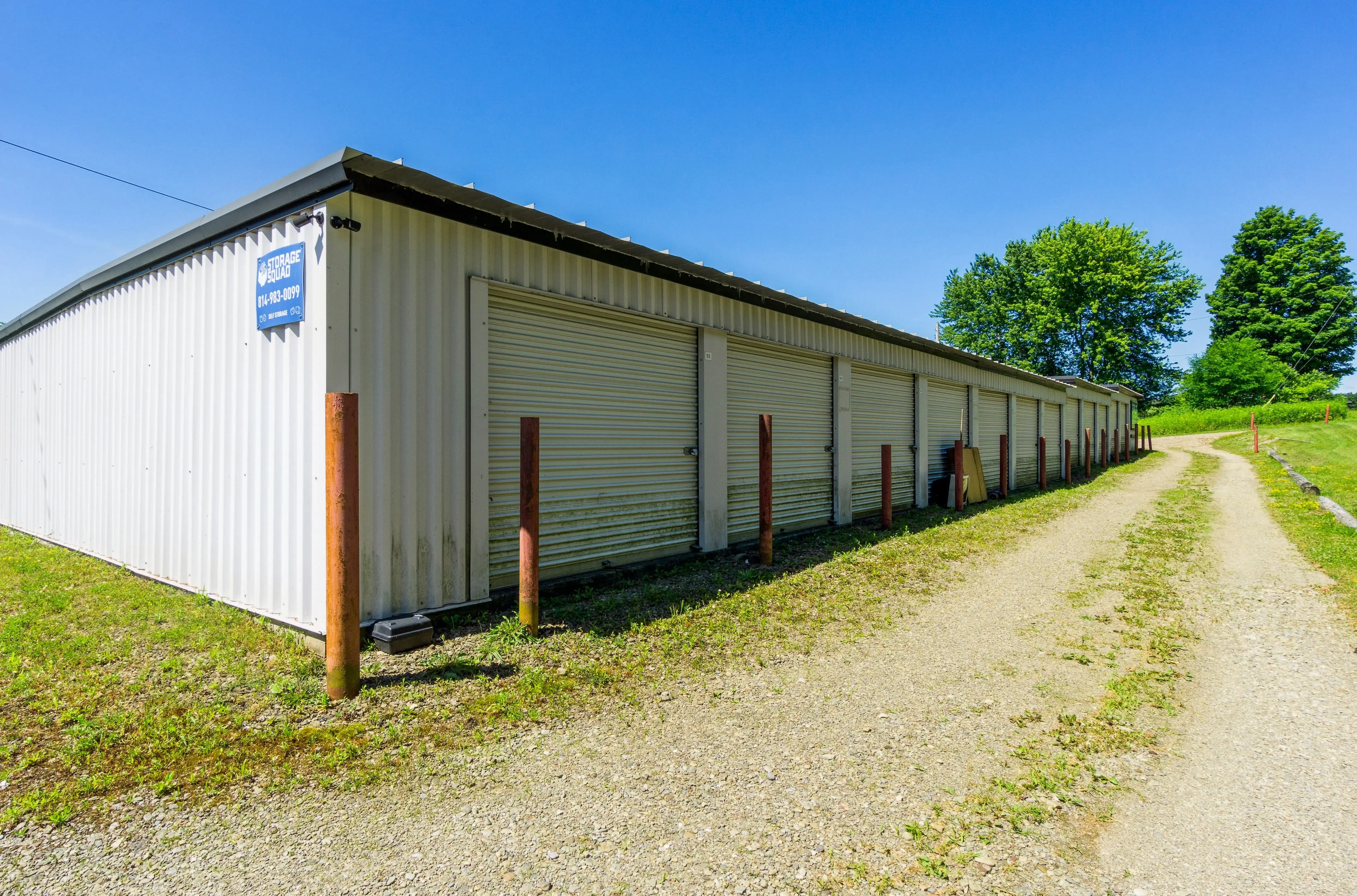 Row of white door storage units along a compact gravel lane bordered by open green space in Union City PA