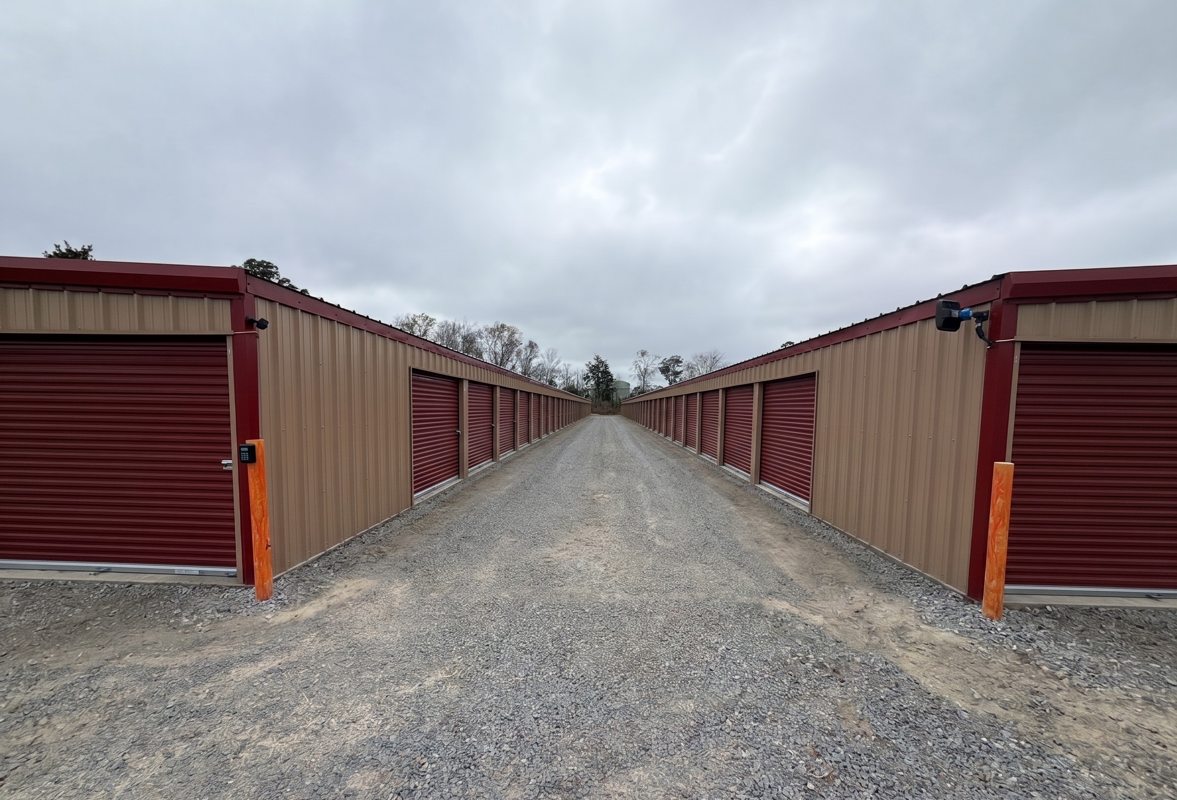 A secure self storage facility in Jesup, GA, showing rows of tan storage units with red roll up doors and gravel paths, perfect for local residents needing extra space or boat storage