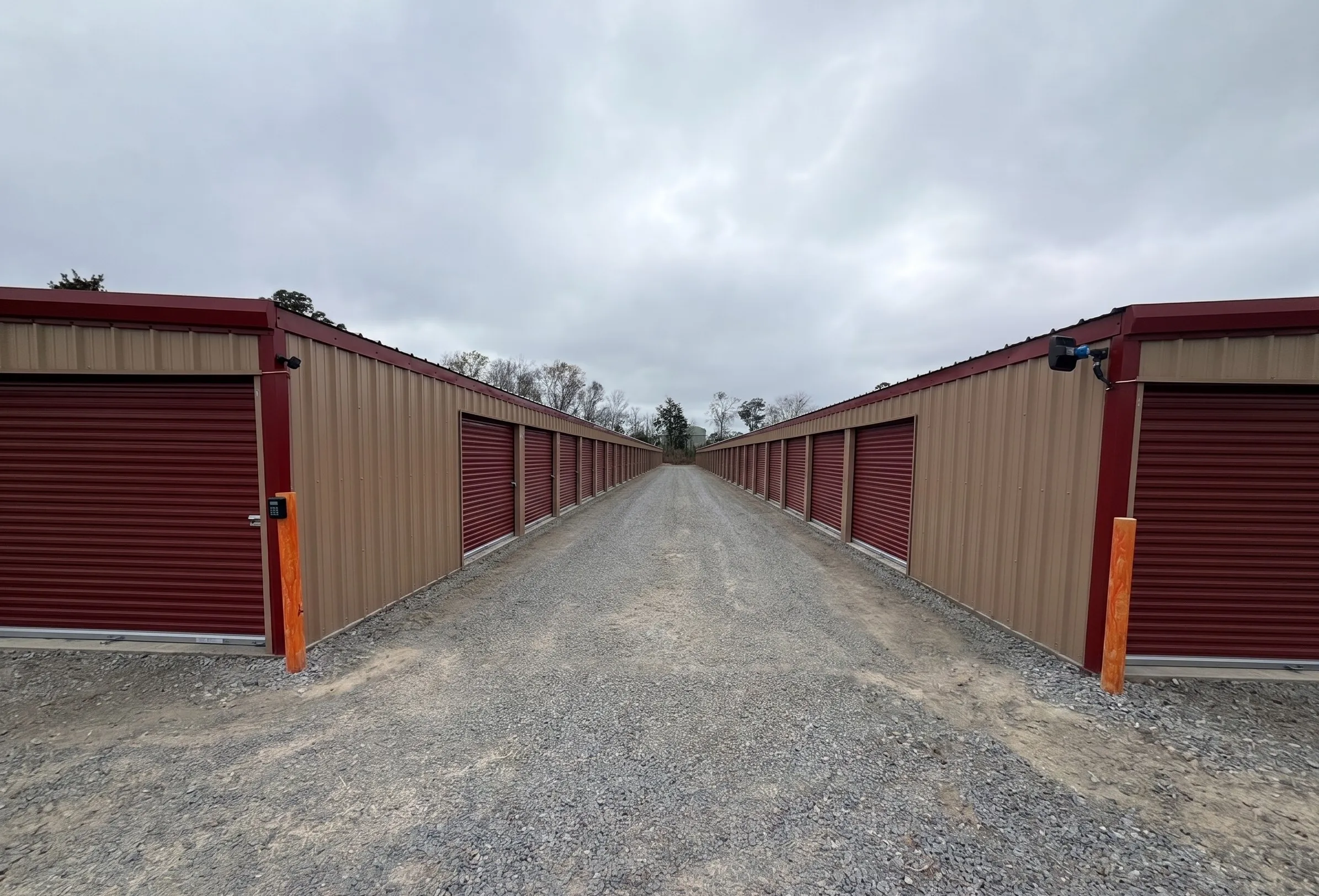 A secure self storage facility in Jesup, GA, showing rows of tan storage units with red roll up doors and gravel paths, perfect for local residents needing extra space or boat storage