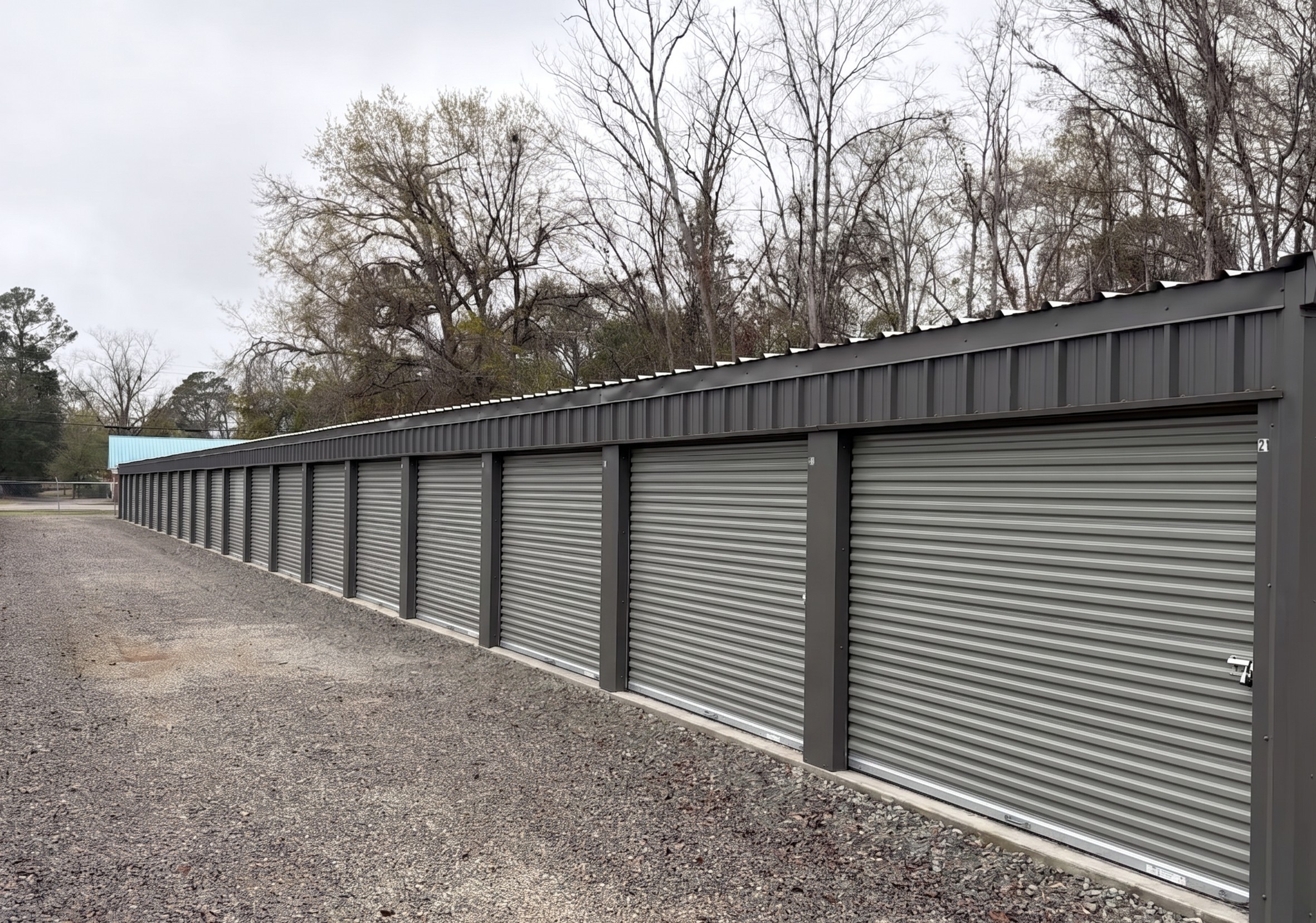 A long row of clean grey self storage units at 540 North Blvd in Baxley, GA, featuring secure metal roll up doors and a wide gravel driveway for easy vehicle access
