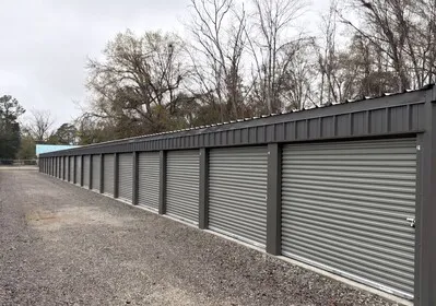 A long row of clean grey self storage units at 540 North Blvd in Baxley, GA, featuring secure metal roll up doors and a wide gravel driveway for easy vehicle access