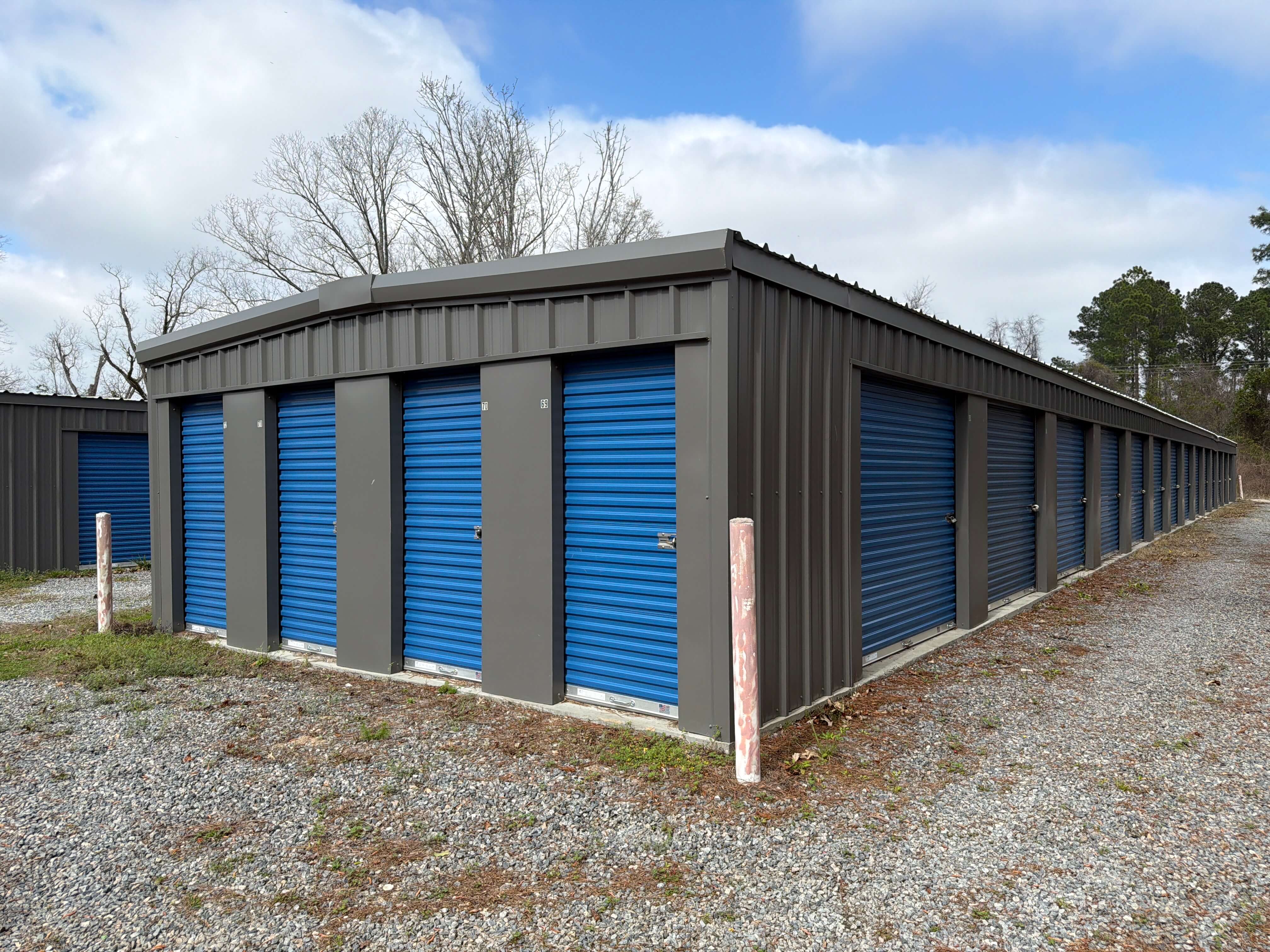 Exterior of a clean self storage building at 1160 W Cherry St in Jesup, GA, featuring bright blue roll up doors and a wide gravel driveway for easy drive-up access