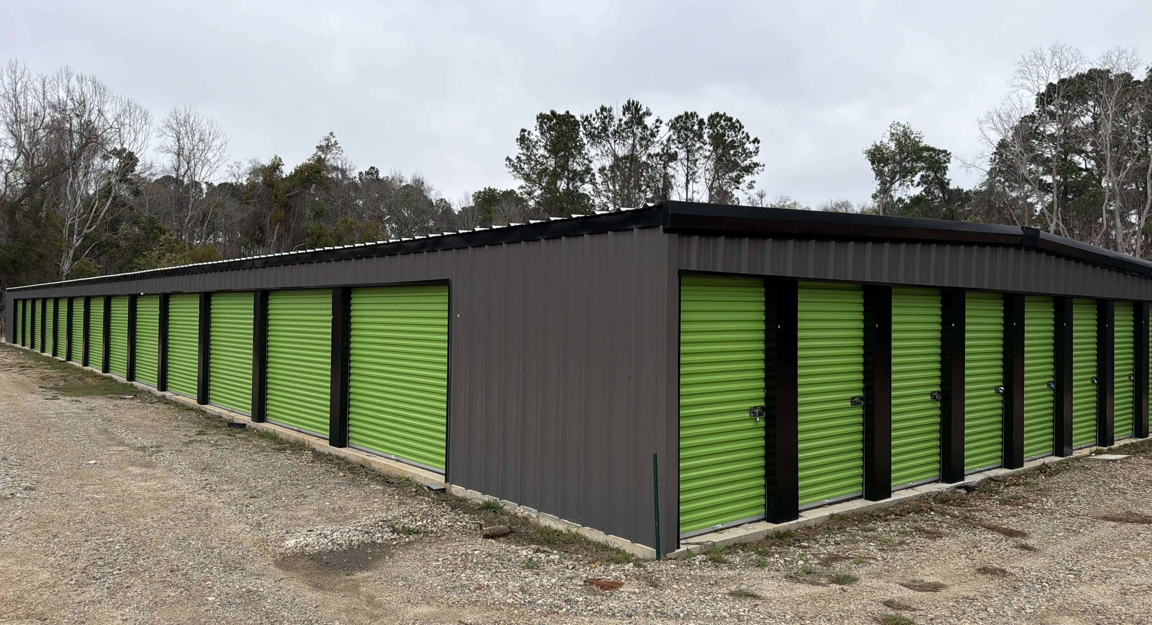 A long perspective shot of a modern storage building at 503 E Carter Ave, featuring several green roll up doors and a spacious gravel path for large trucks and trailers
