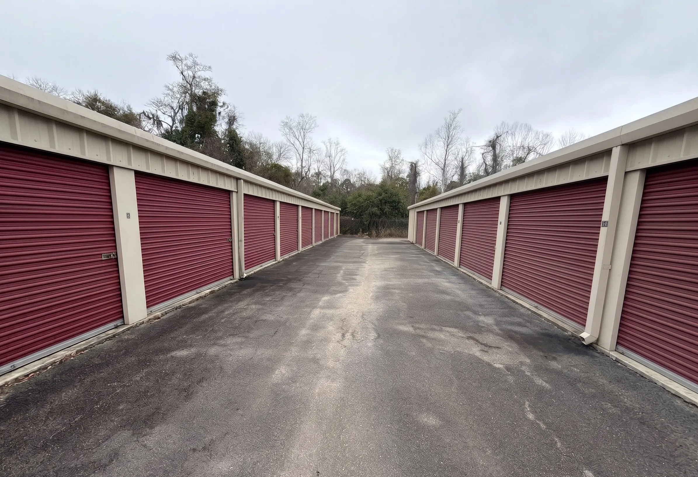Looking down a paved lane between two rows of self storage units in Blackshear, GA 31516, featuring tan buildings with secure red roll up doors on both sides.