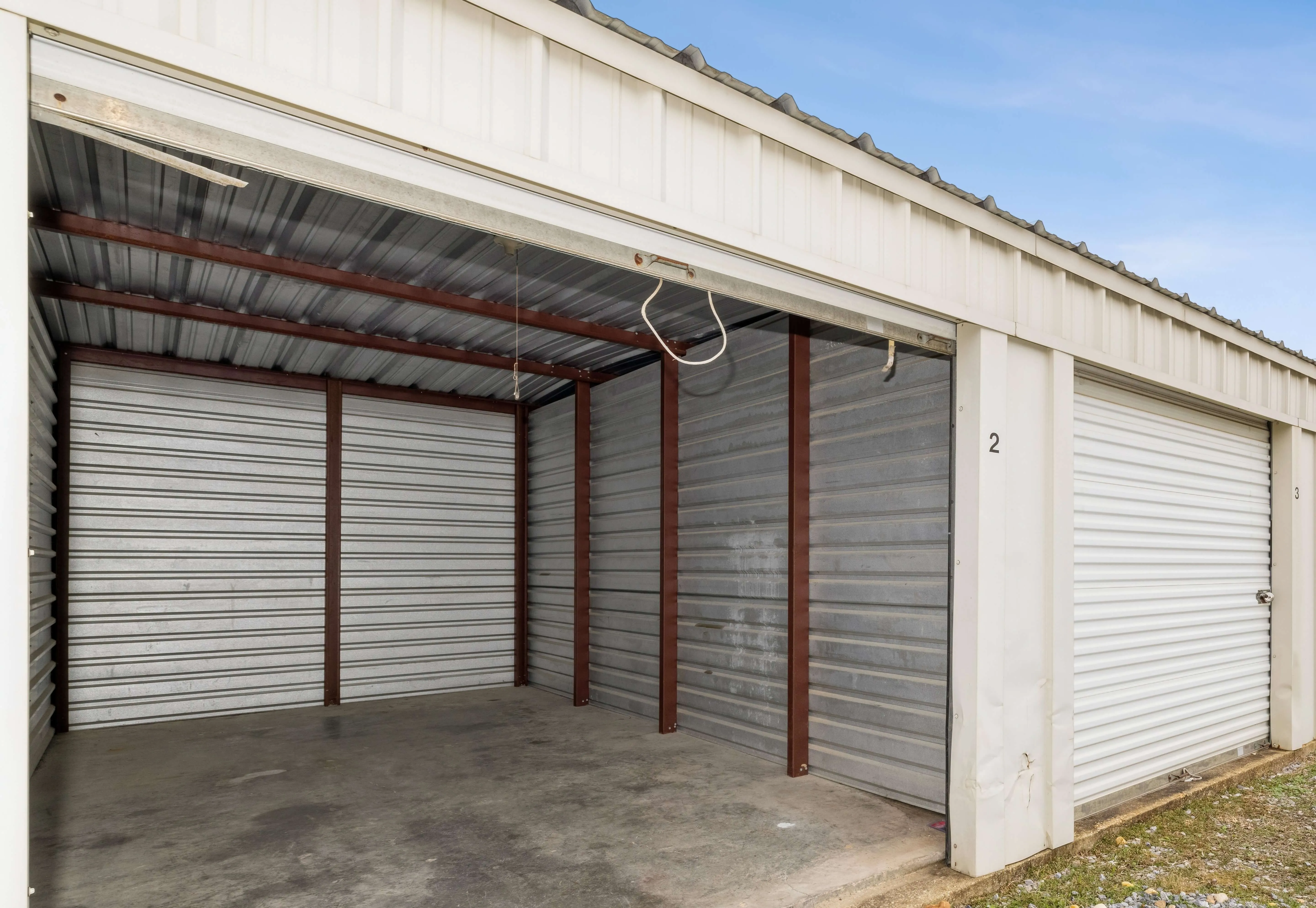 Open, empty drive-up storage unit with its white roll-up door raised at Bolt Storage in Pensacola, FL, showing a clean concrete floor and metal walls