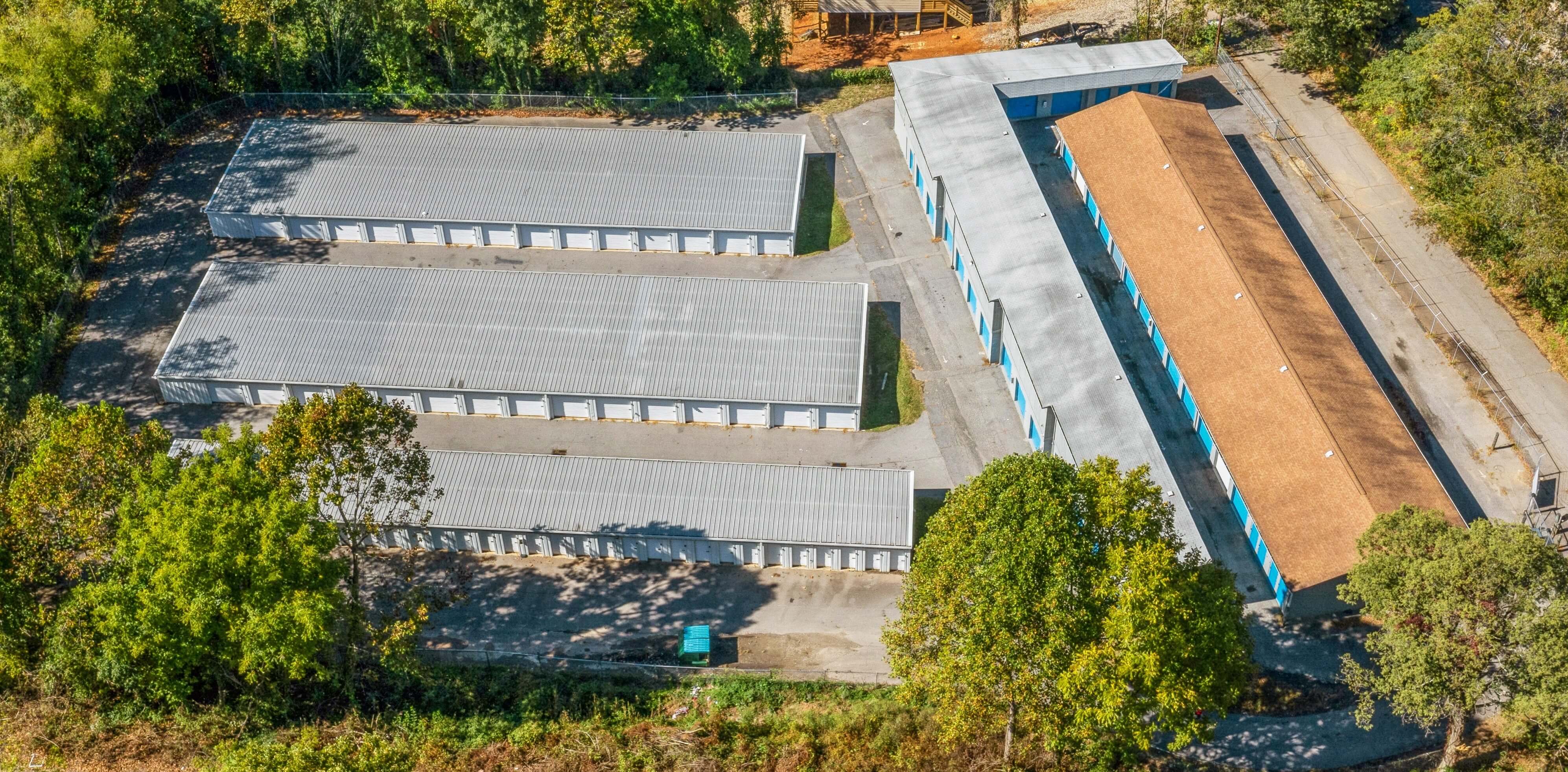 Aerial view of the Bolt Storage facility in West Asheville, NC, showing several long rows of single-story drive-up storage units with blue and white doors, surrounded by trees