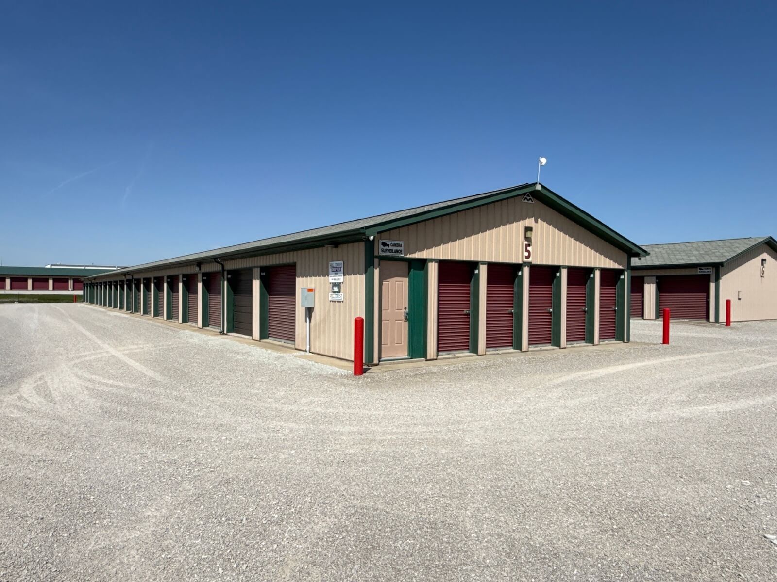Corner view of a self storage building with burgundy doors and a drop-box sign at Bolt Storage in Ossian, IN