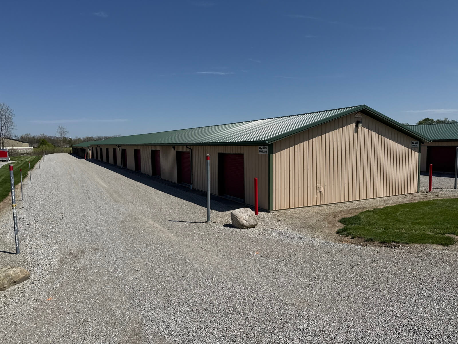 Exterior view of a tan self storage building with green roof and burgundy unit doors at Bolt Storage in Ossian, Indiana