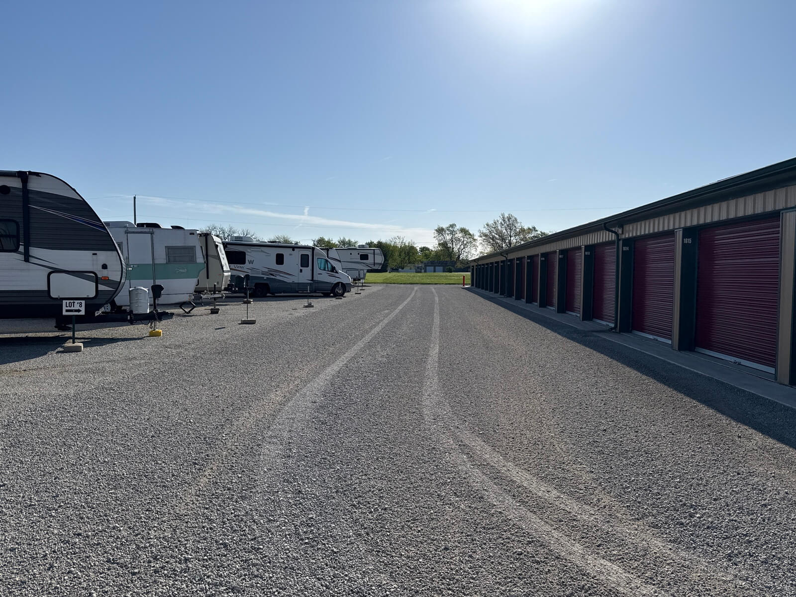 Outdoor RV and trailer parking spaces beside a self storage building with burgundy roll-up doors at Bolt Storage Ossian, IN
