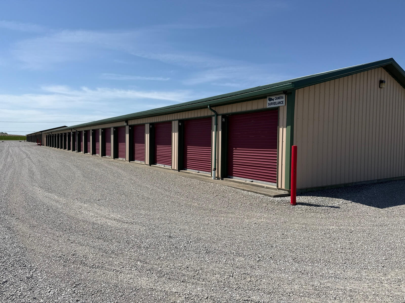 Row of drive-up self storage units with burgundy doors at Bolt Storage Ossian, IN, off a gravel access road