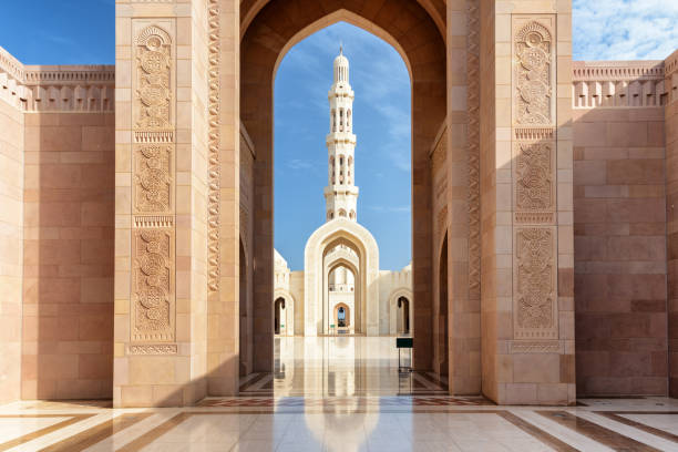 View through ornate archway of a tall white minaret against a blue sky at a marble courtyard mosque.