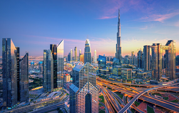 Aerial view of Dubai skyline at sunset featuring Burj Khalifa and illuminated highways.