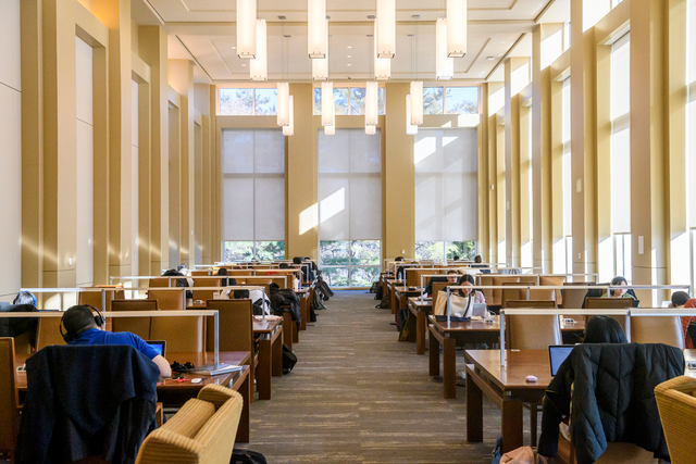 Bright, spacious reading room with tall windows, rows of study desks, and people working quietly.