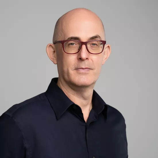 Middle-aged bald man with glasses wearing a black button-up shirt against a gray background.