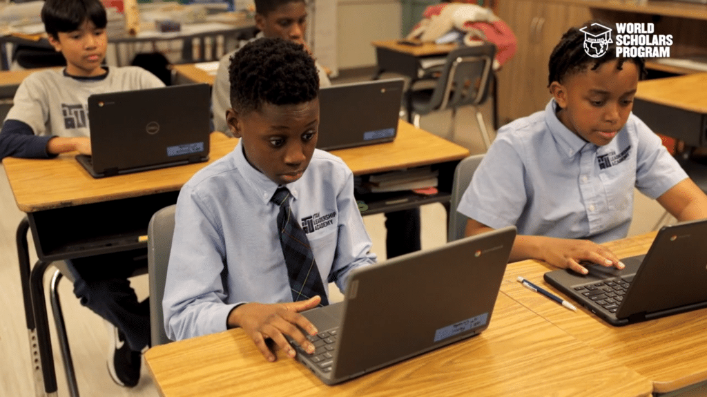 Four students in a classroom working on laptops, wearing school uniforms with ties and concentrating on their screens.