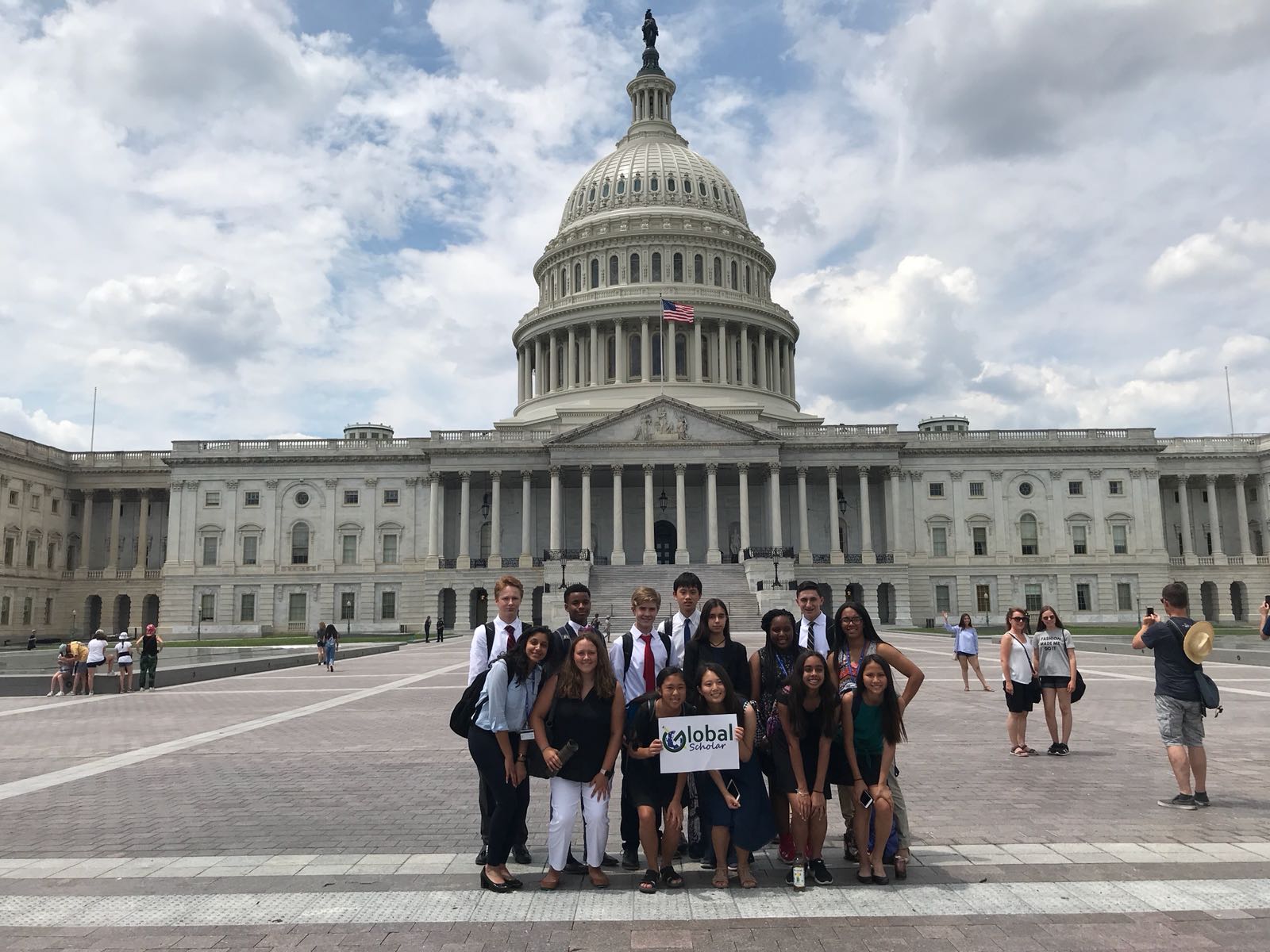 Group of young people posing with a Global Scholar sign in front of the U.S. Capitol building on a partly cloudy day.