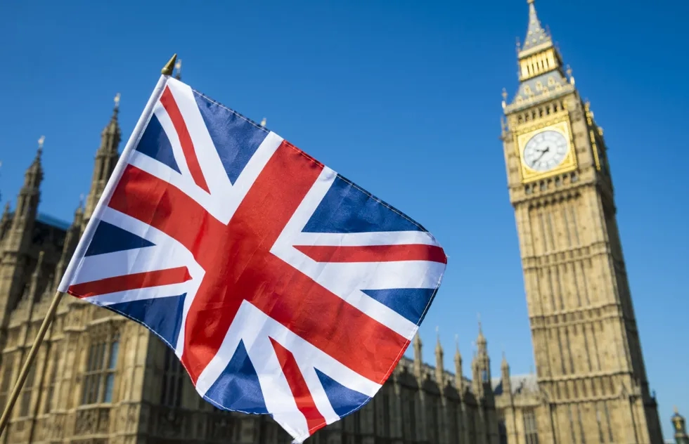 Union Jack flag waving in front of the Elizabeth Tower with Big Ben clock in London on a clear blue sky day.
