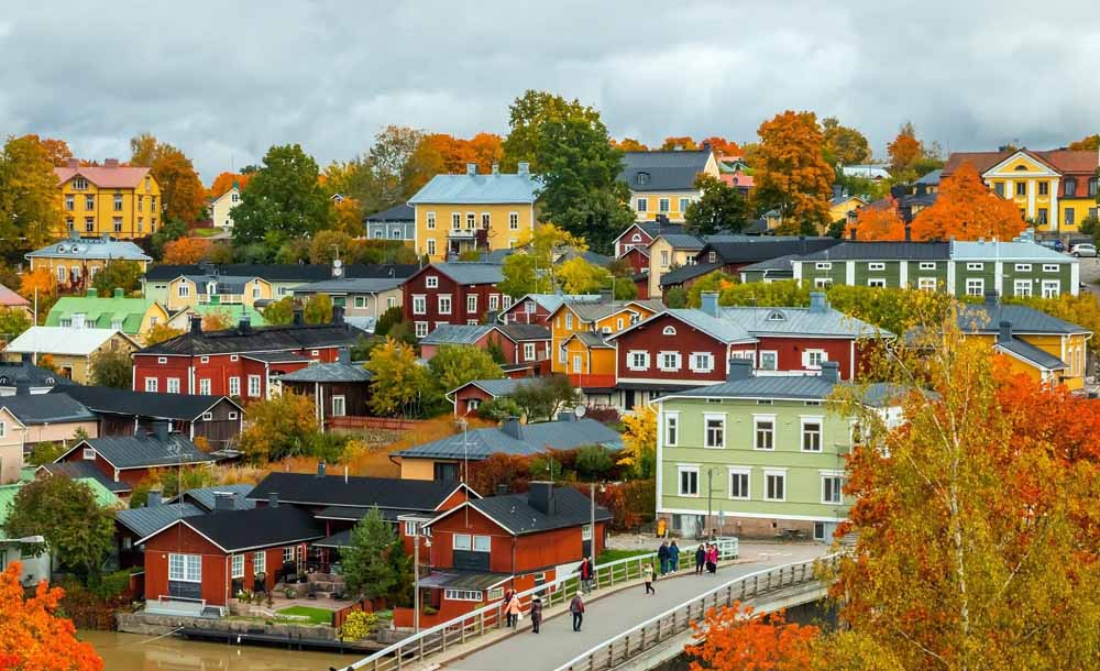Colorful traditional wooden houses in a Finnish town during autumn with orange and yellow foliage and people walking on a bridge.