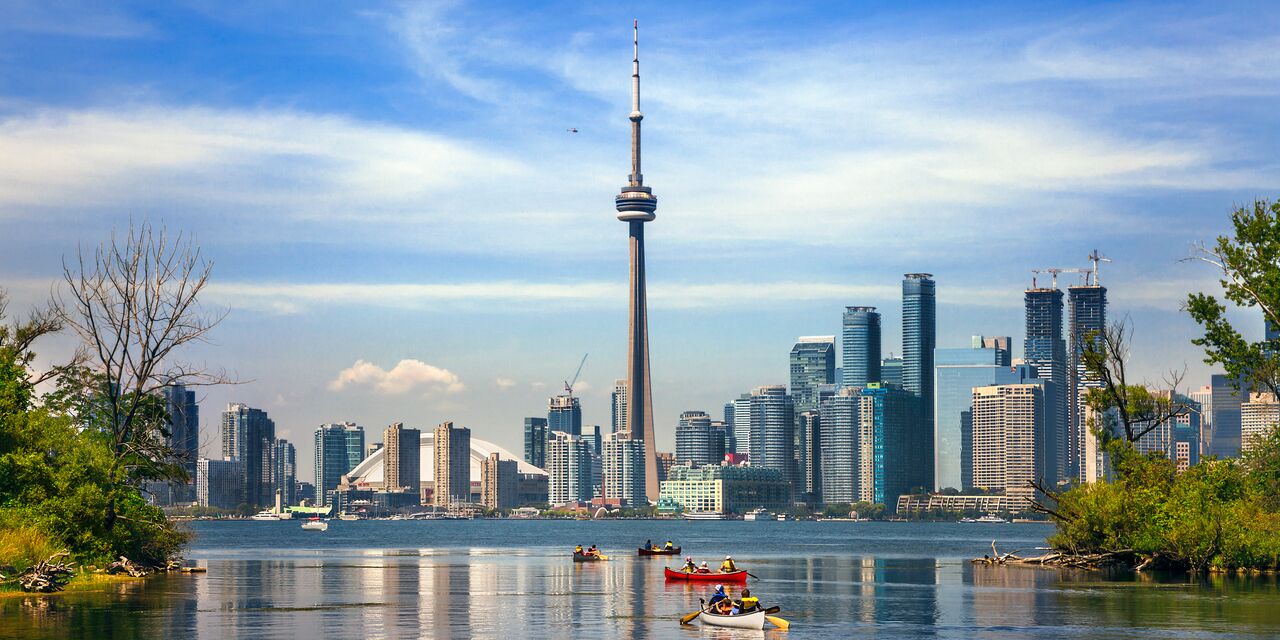 Toronto skyline with CN Tower and people kayaking on Lake Ontario under a blue sky.