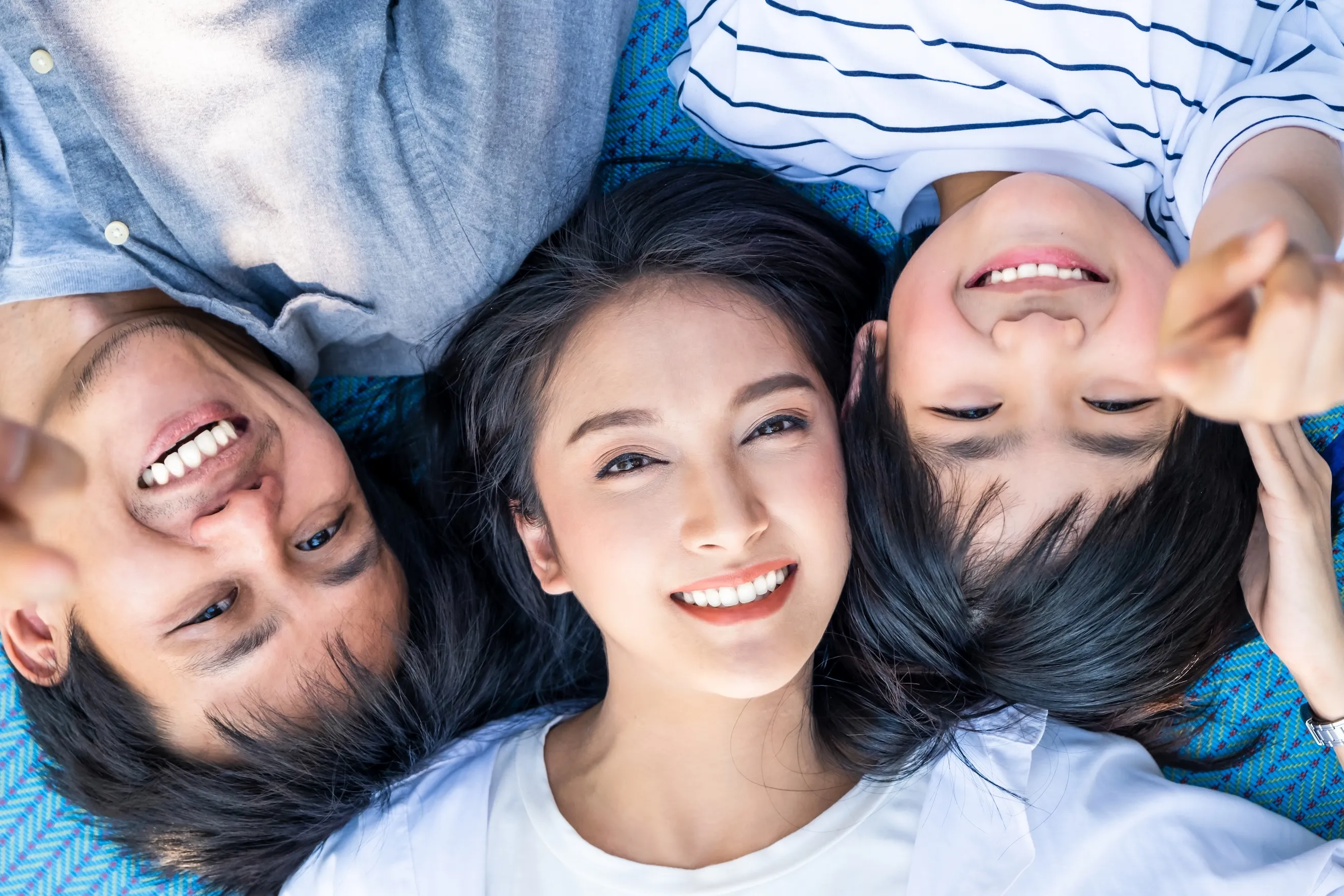 Smiling family of three lying on a blue patterned blanket with heads close together.