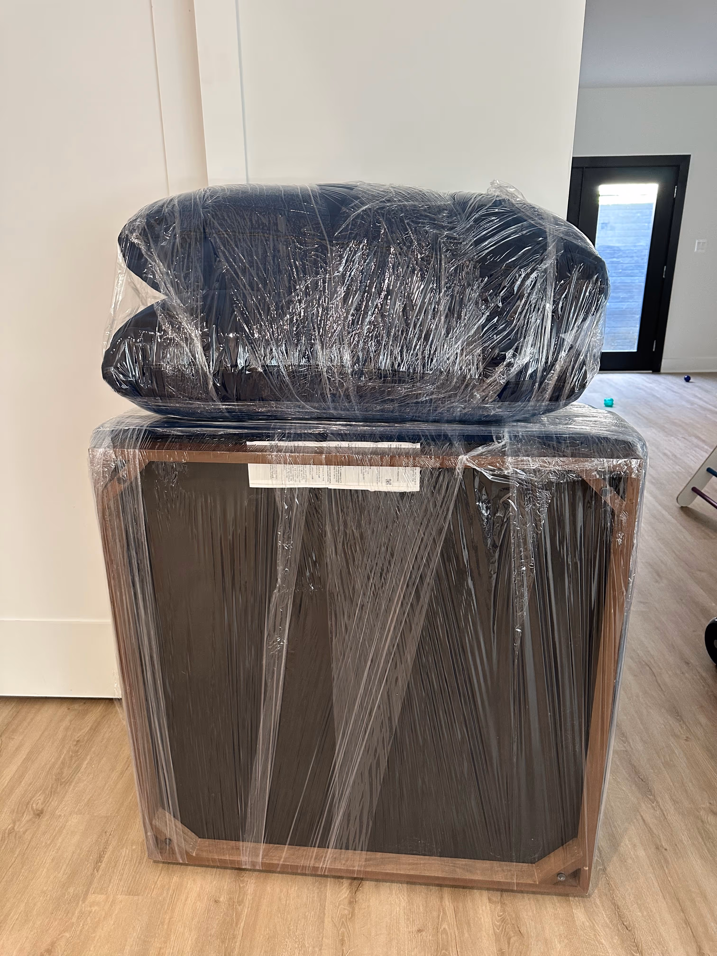 Two pieces of furniture wrapped in clear plastic wrap placed on a wooden floor inside a room.