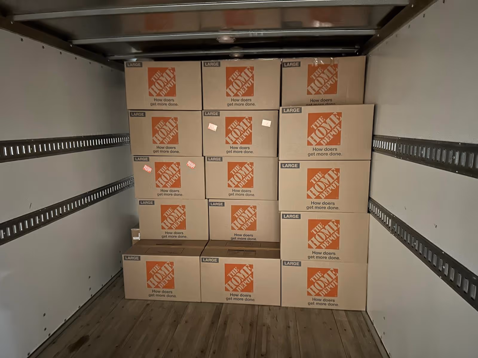 Stack of large Home Depot moving boxes neatly arranged inside a truck with wooden floor.
